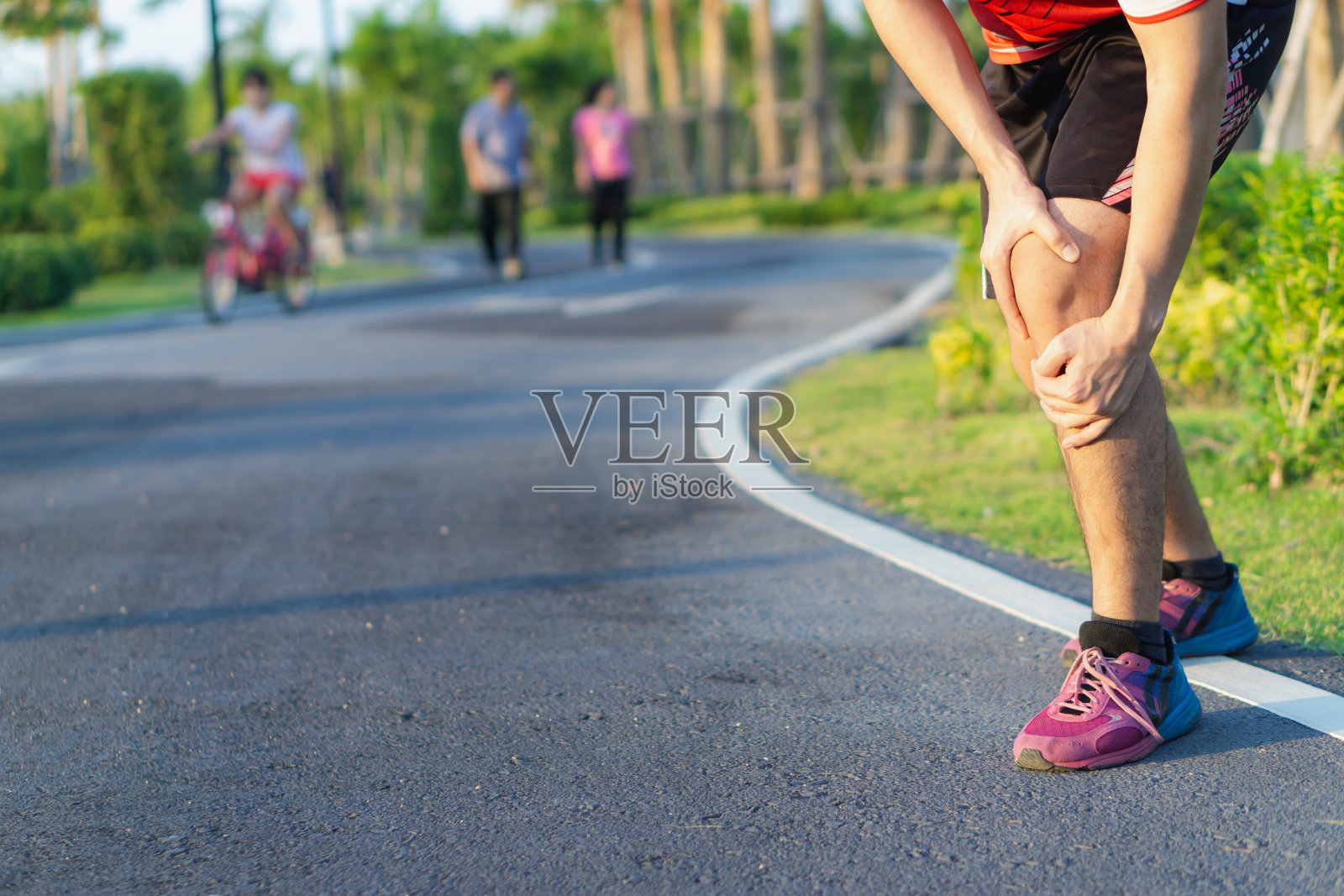 膝盖受伤。一名年轻的运动员在公园跑步锻炼时肌肉受伤，双手抱着膝盖，疼痛难忍。保健和运动概念。照片摄影图片