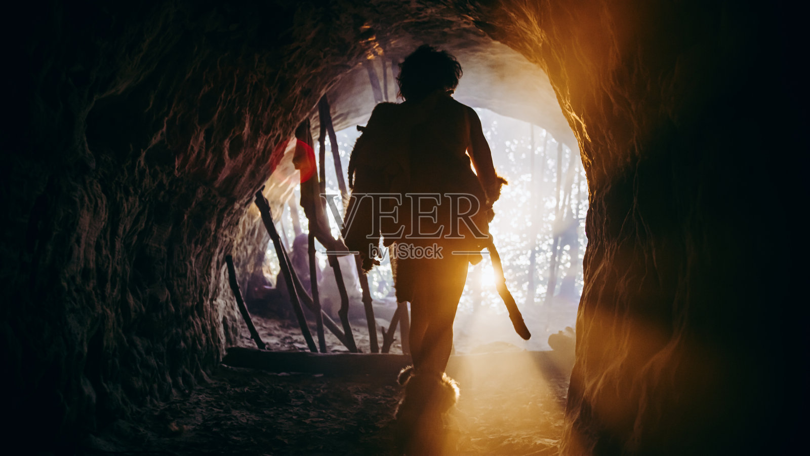 原始穴居人在动物的皮肤和皮毛持有石头尖头矛走出他的洞穴进入史前森林准备狩猎。尼安德特人进入丛林狩猎。用暖滤镜拍摄。照片摄影图片