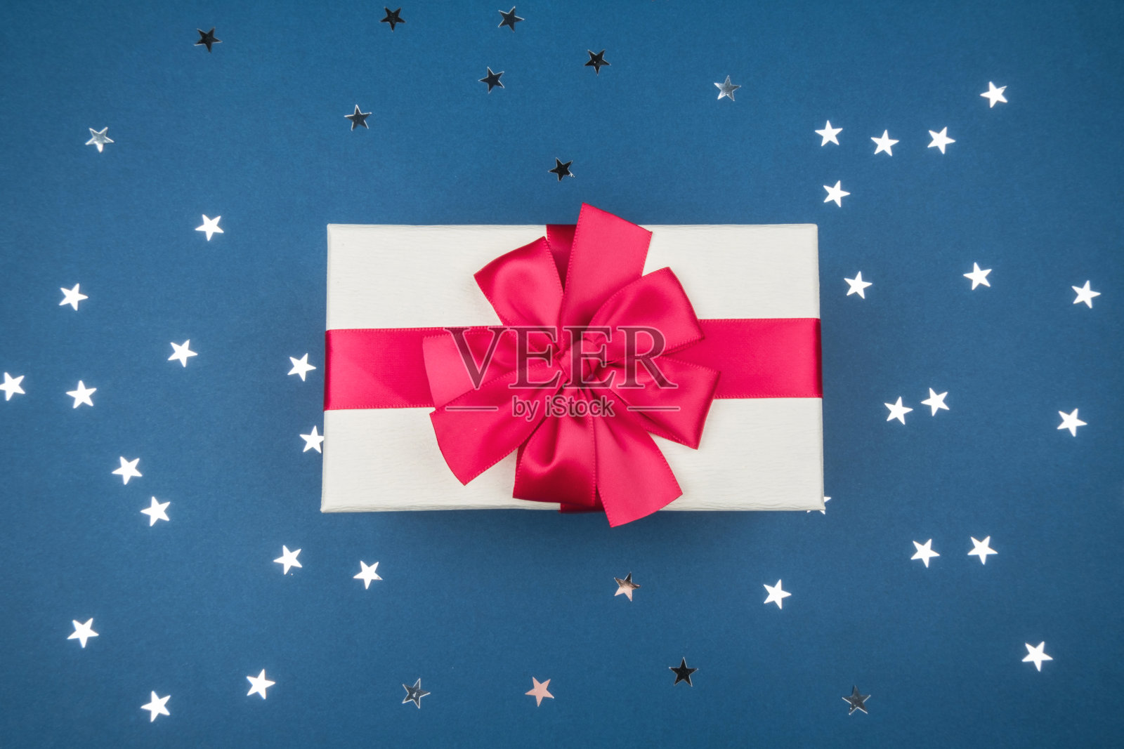 礼盒与红色蝴蝶结在蓝色背景与银星。照片摄影图片