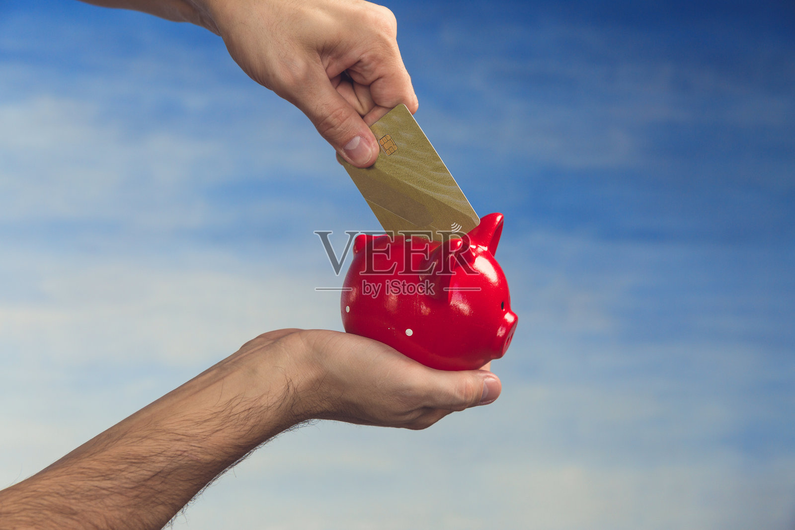 一个男人的手正试图往储蓄罐里塞一张信用卡。照片摄影图片