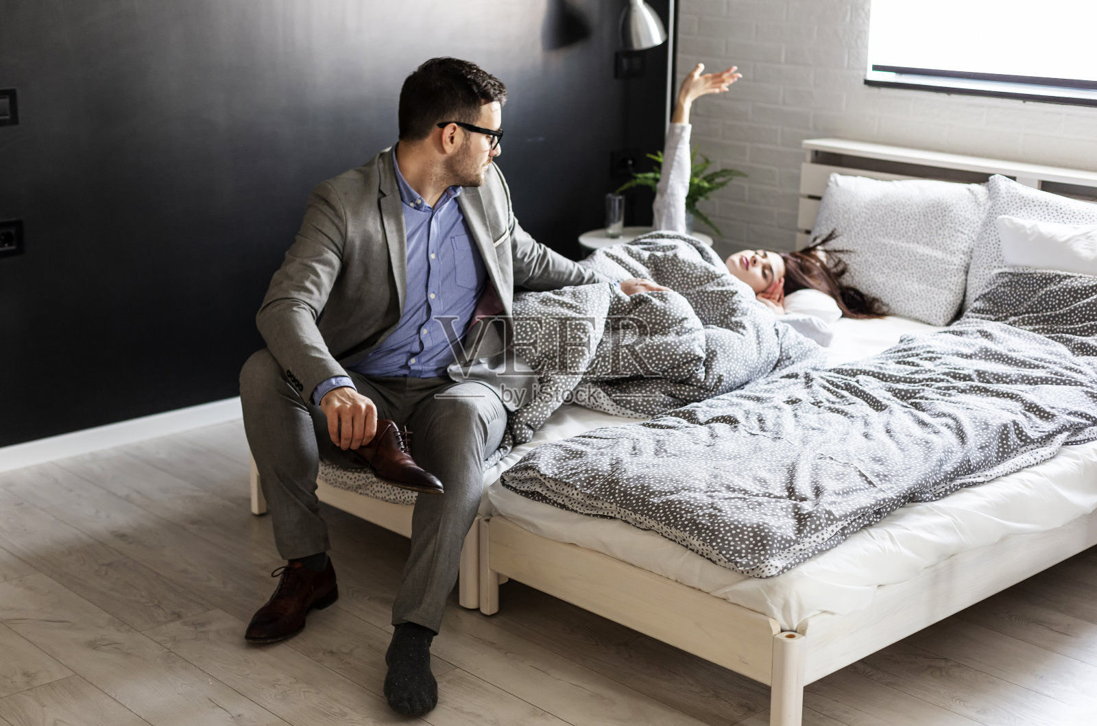 夫妻俩在卧室里西装革履准备上班，而她则穿着睡衣躺在床上醒来照片摄影图片