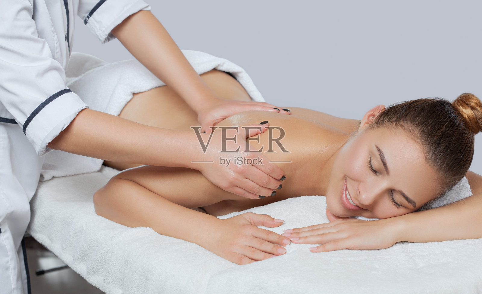 按摩师让一个年轻美丽的女人在水疗中心的脸，脖子，肩膀，背部和锁骨放松按摩。美容和按摩概念。照片摄影图片