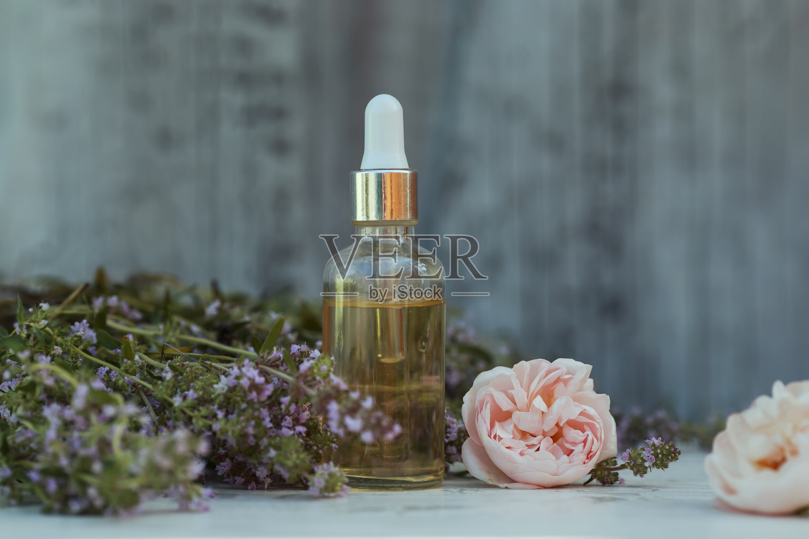 在一个阳光明媚的花园里，化妆瓶、吸管、薰衣草和玫瑰油放在一张木桌上，旁边是精致的紫丁香和粉红色的芳香花朵照片摄影图片