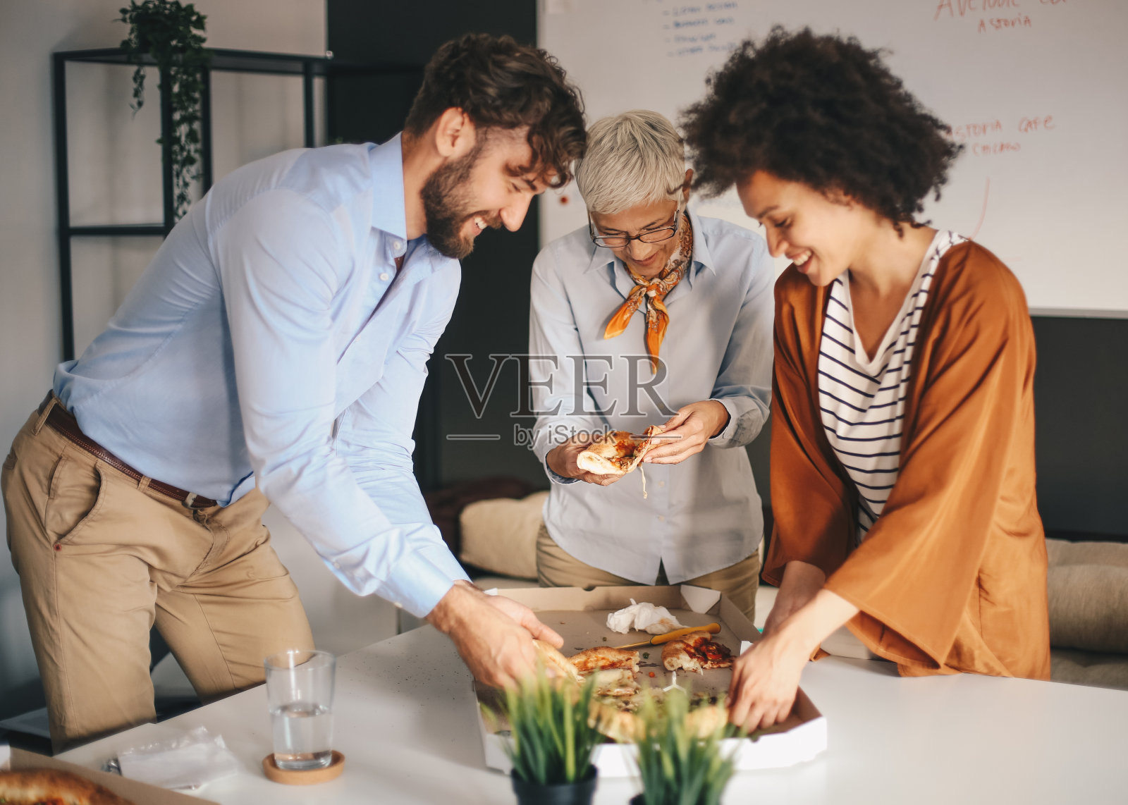 一个经理和两个年轻的员工在一起吃披萨。照片摄影图片