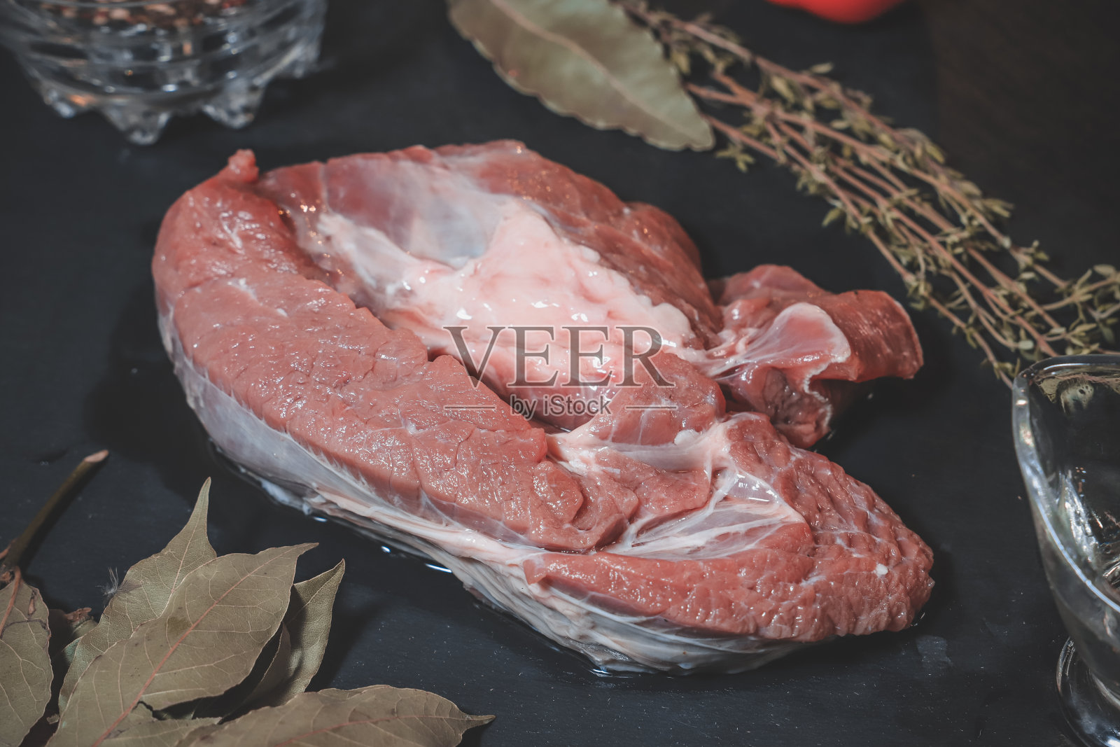 在一个石墨色的石头架子上，放着一块鲜亮的生牛肉，上面点缀着青椒豌豆照片摄影图片