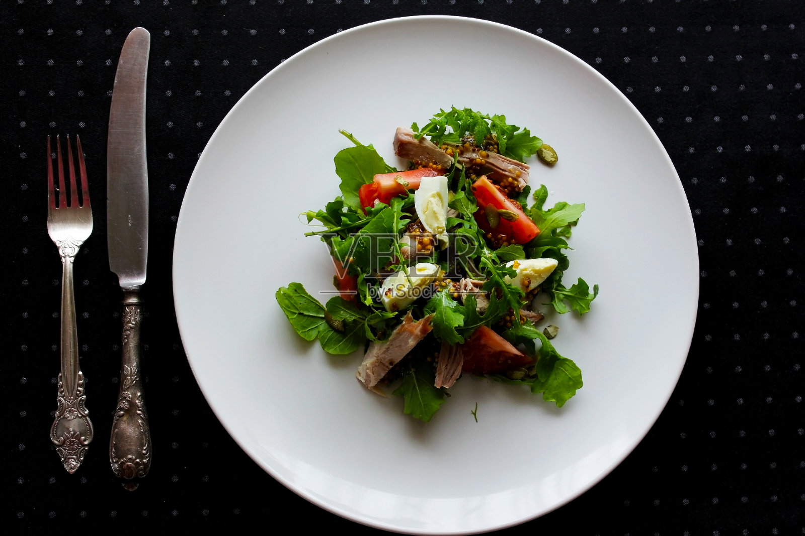 新鲜蔬菜沙拉盘西红柿，菠菜，胡椒，芝麻菜，金枪鱼。健康食品。节食晚餐或午餐菜单。沙拉盘在桌上。平的。从上面的观点照片摄影图片