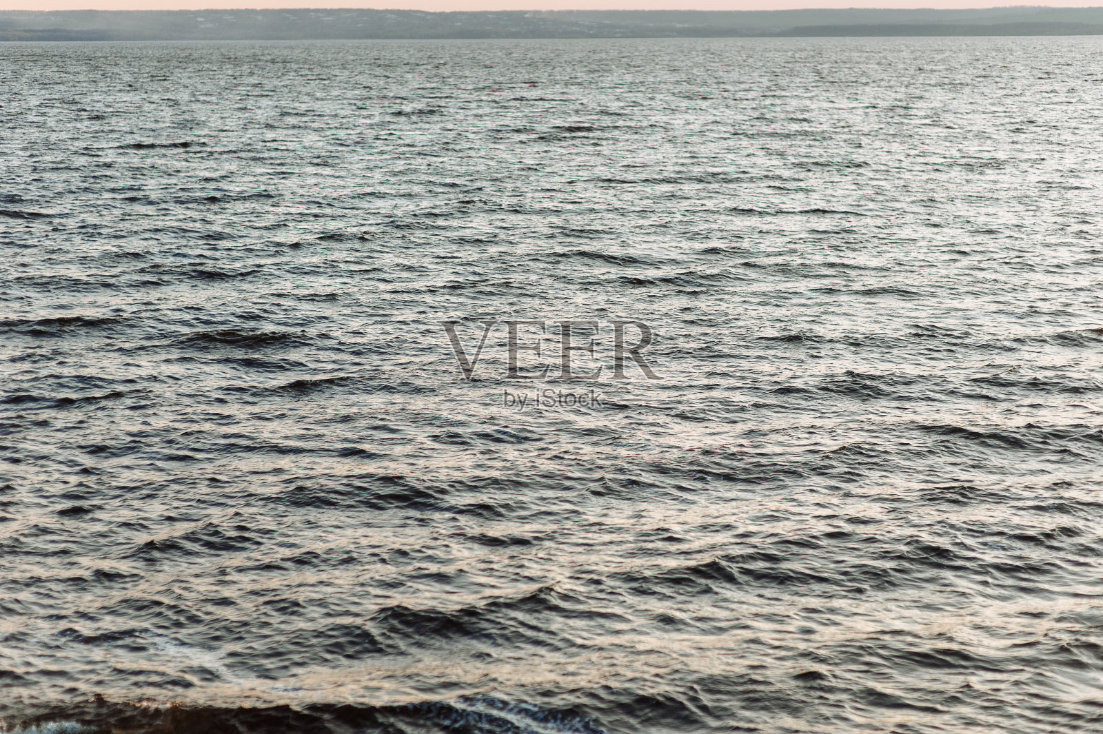 汹涌的江海为背景。日落时的小波浪。照片摄影图片