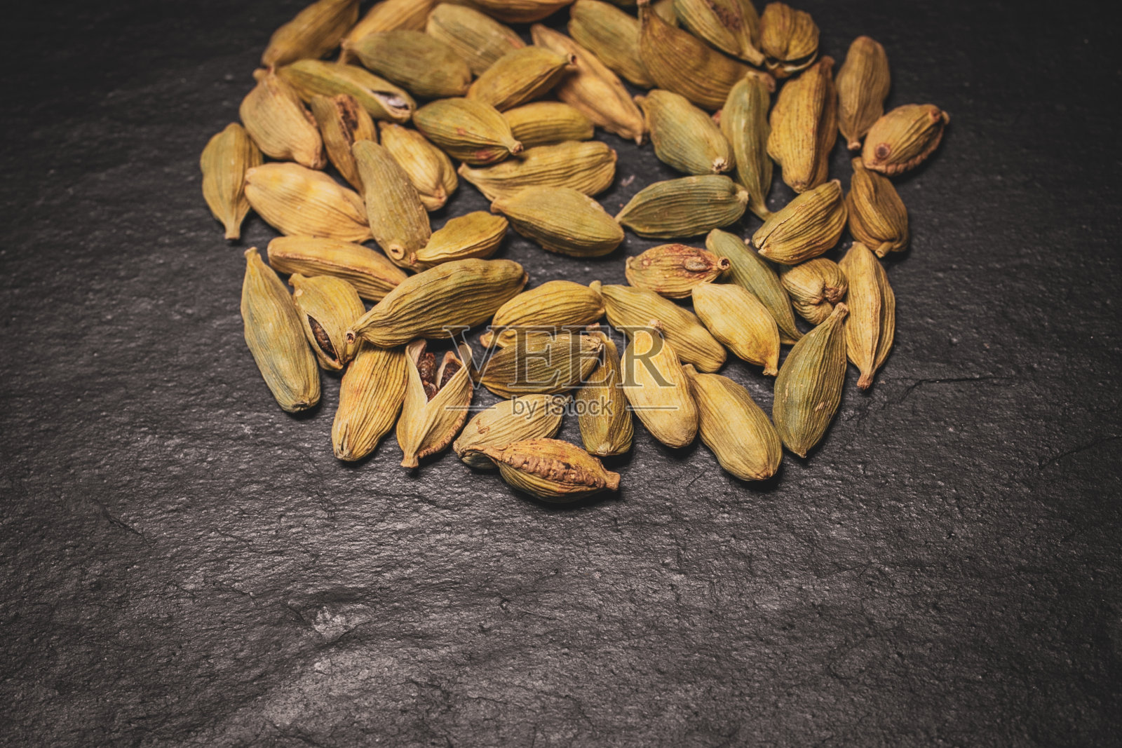 堆绿色豆蔻种子在黑色石板背景近距离观看。有机健康食品。世界香料。照片摄影图片
