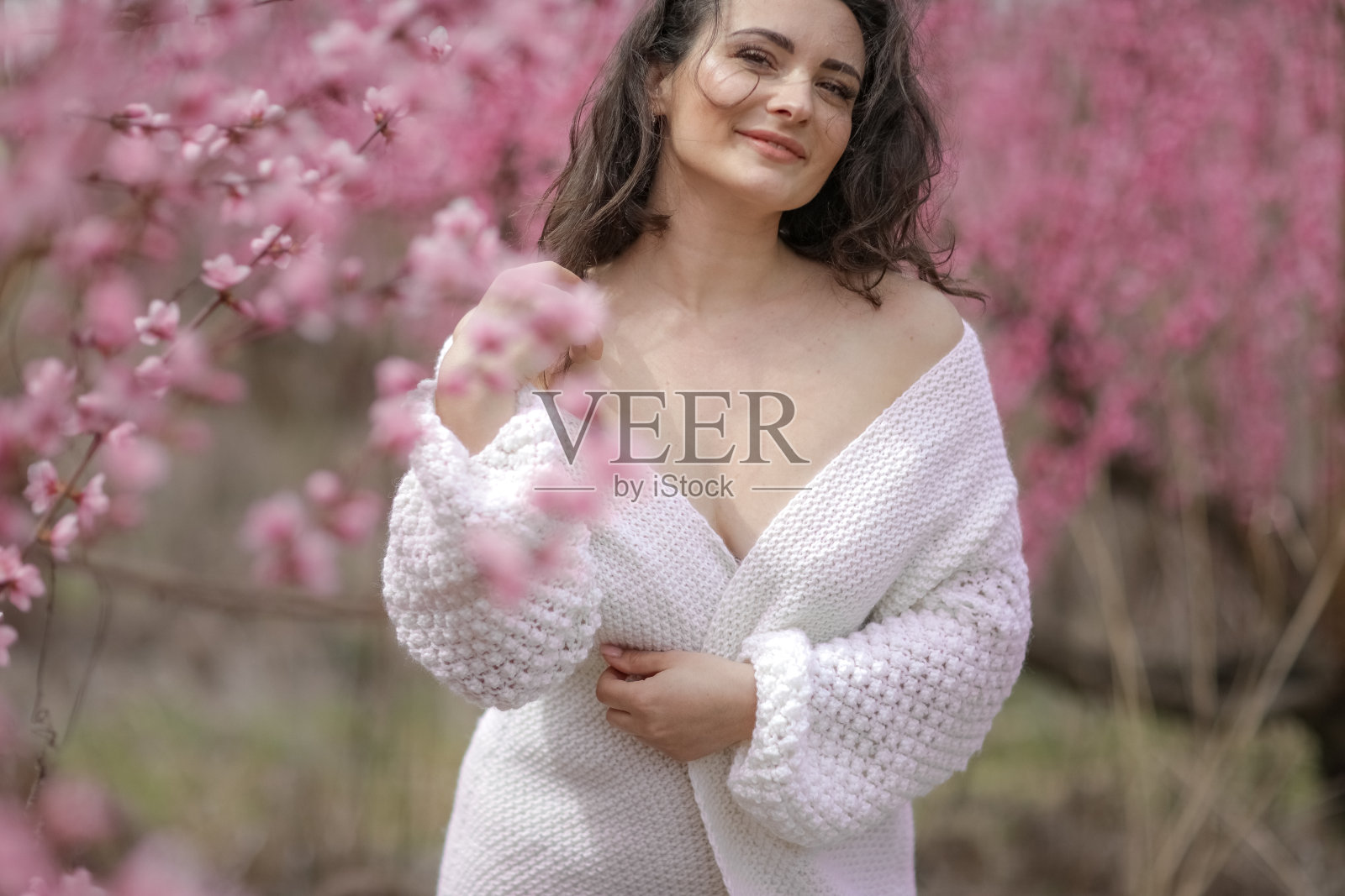 一个美丽的成年女人赤裸着肩膀，穿着毛衣，背景是一个开花的桃园照片摄影图片