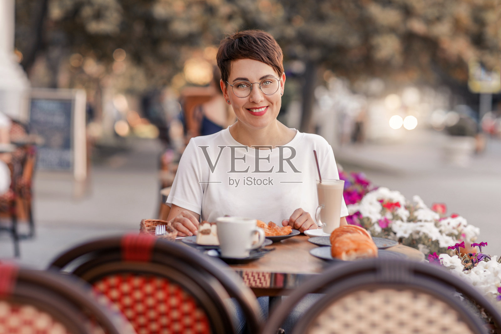 一个度假的女人在咖啡馆里喝着奶昔，吃着羊角面包照片摄影图片