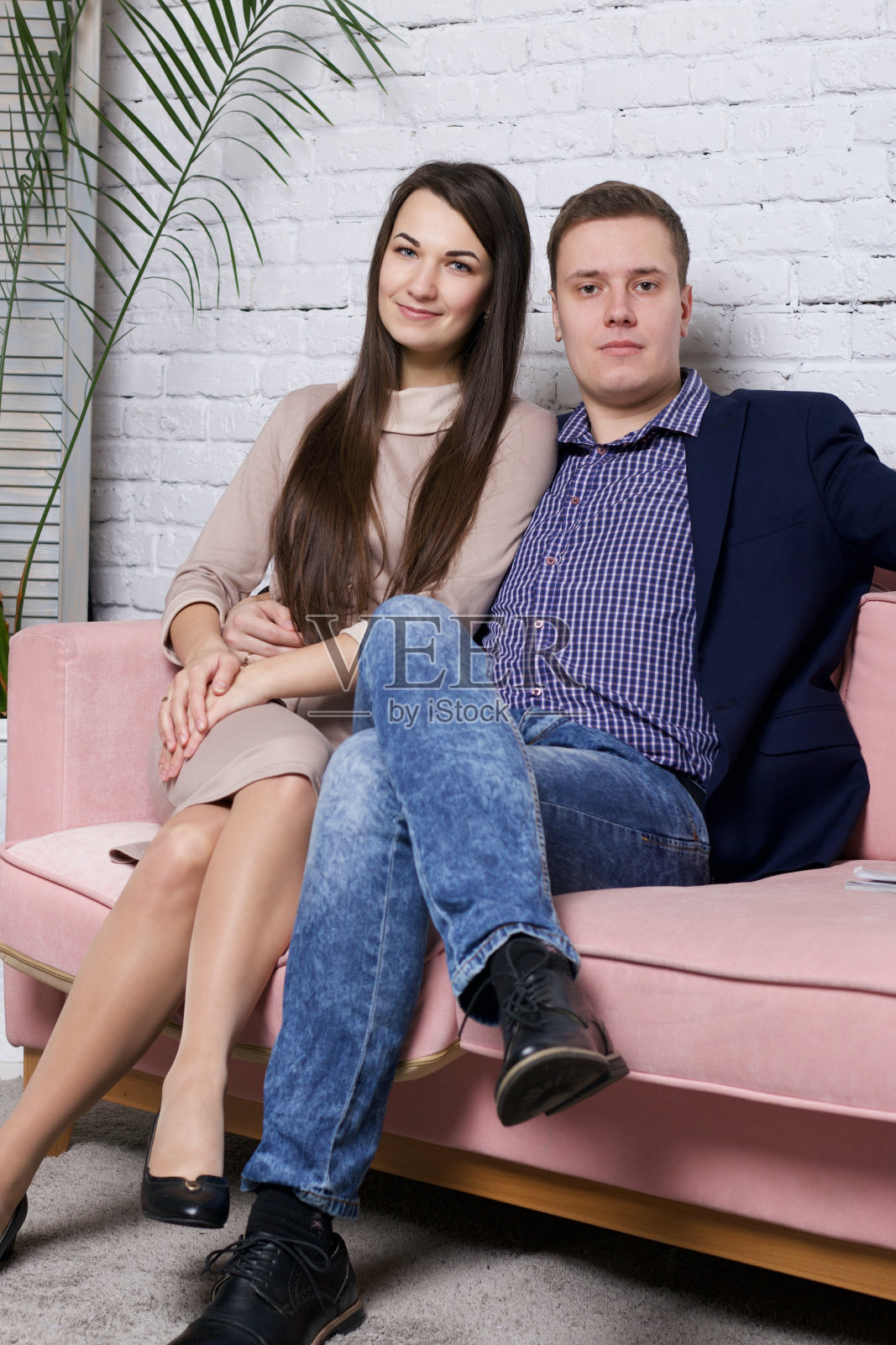 一个年轻的家庭正坐在沙发上。包厢里穿着。快乐的心情。旁边的花盆里有一棵棕榈树。照片摄影图片