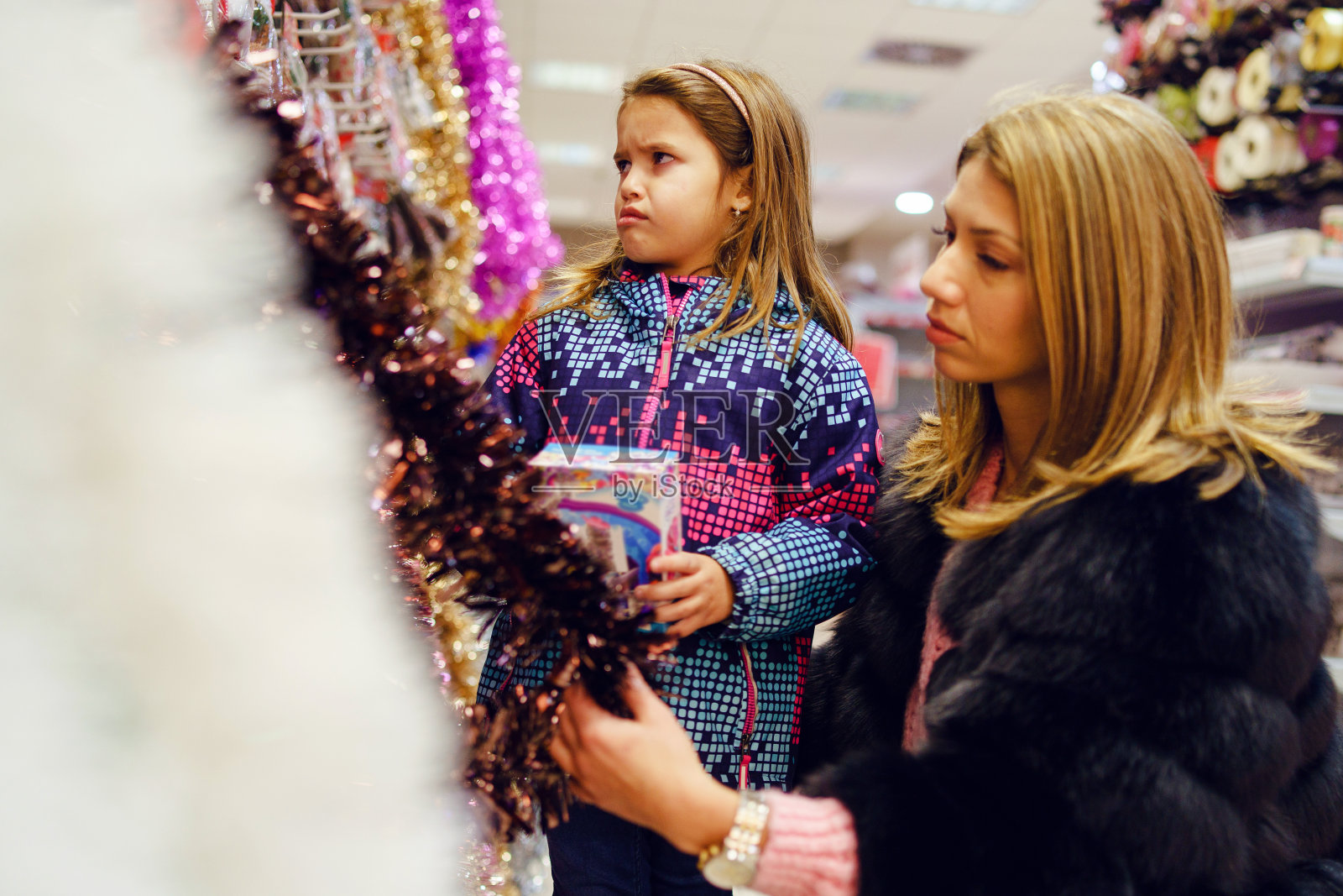 小女孩和她的母亲、妇女和孩子在市场商店的货架旁挑选玩具和装饰品照片摄影图片