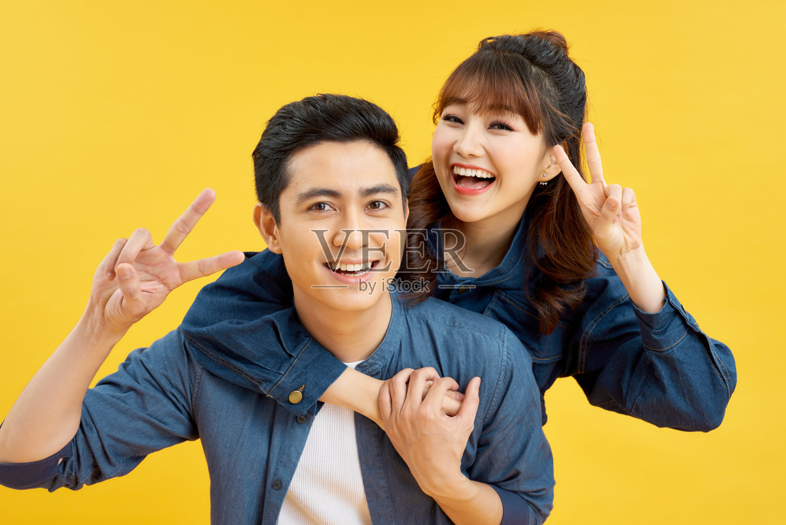 一个快乐的男人背着他的女朋友，伸出两根手指照片摄影图片