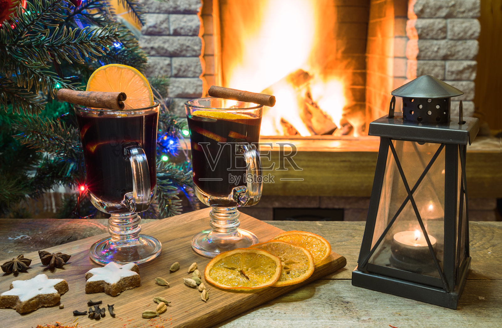 在燃烧的壁炉和新年树前，在木板上放两杯热葡萄酒。照片摄影图片