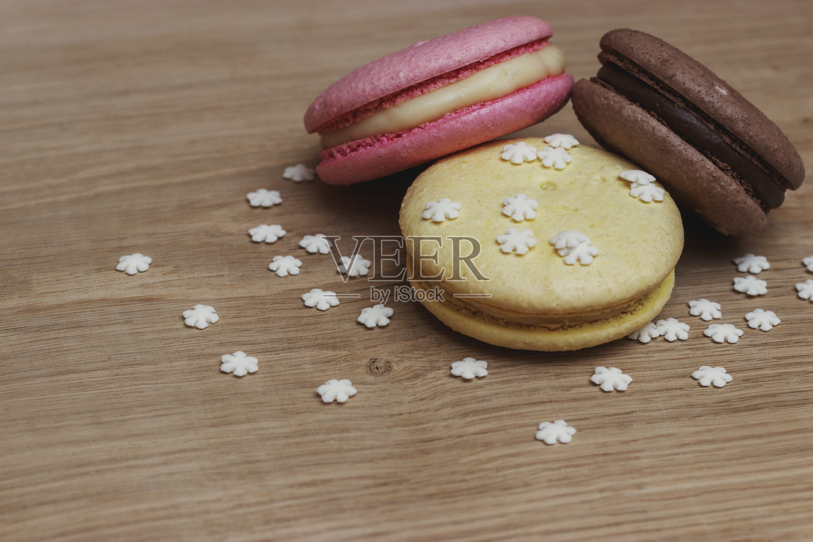 在白橡木板上撒上雪花糖果装饰的彩色杏仁饼干糕点。照片摄影图片