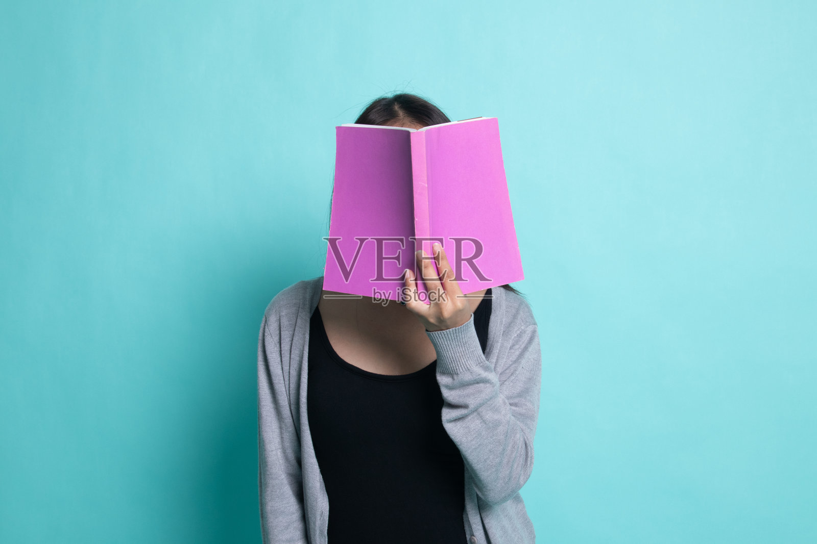 年轻的亚洲妇女用一本书遮住她的脸。照片摄影图片