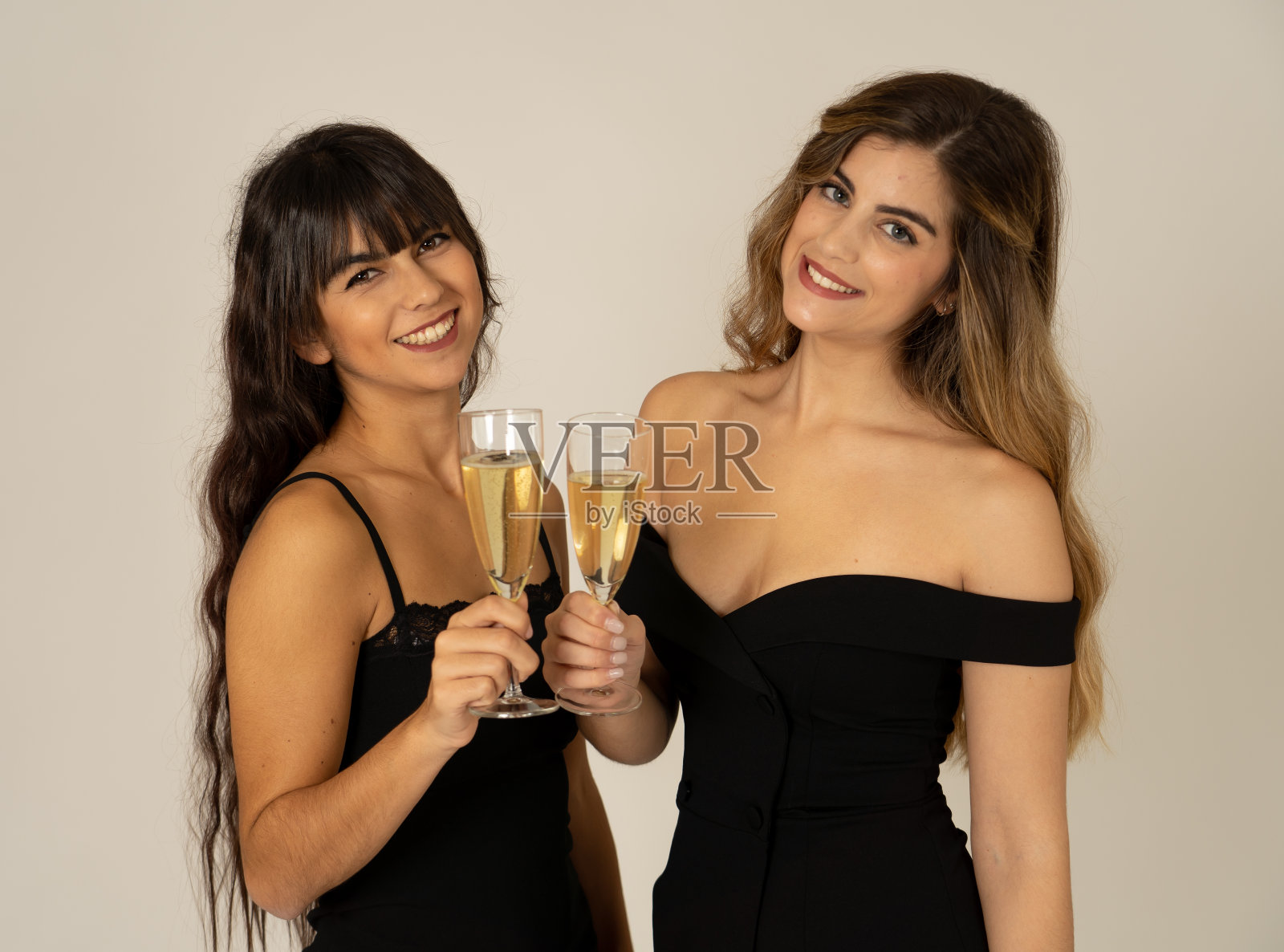 两个美丽的女朋友开心地庆祝圣诞节或新年前夜举杯祝酒。女性们穿着时尚性感的派对礼服，喝着香槟。人们的友谊和庆祝。照片摄影图片