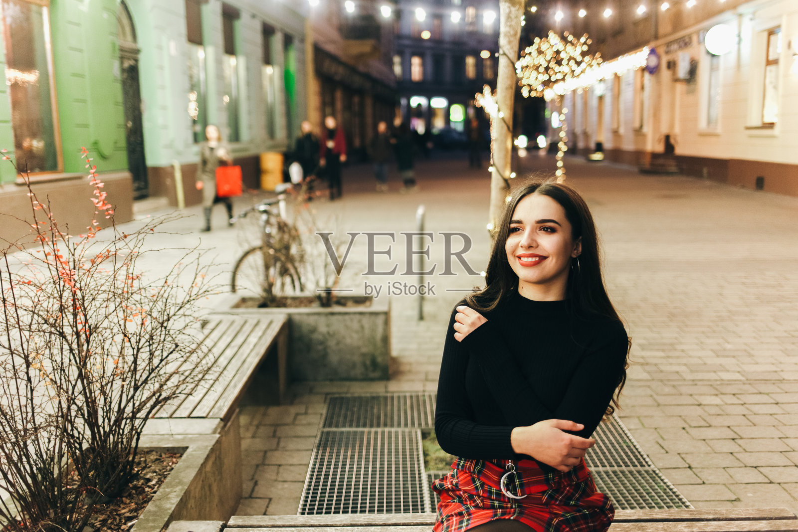 美丽的女孩坐在夜晚装饰着圣诞彩灯的街道上照片摄影图片