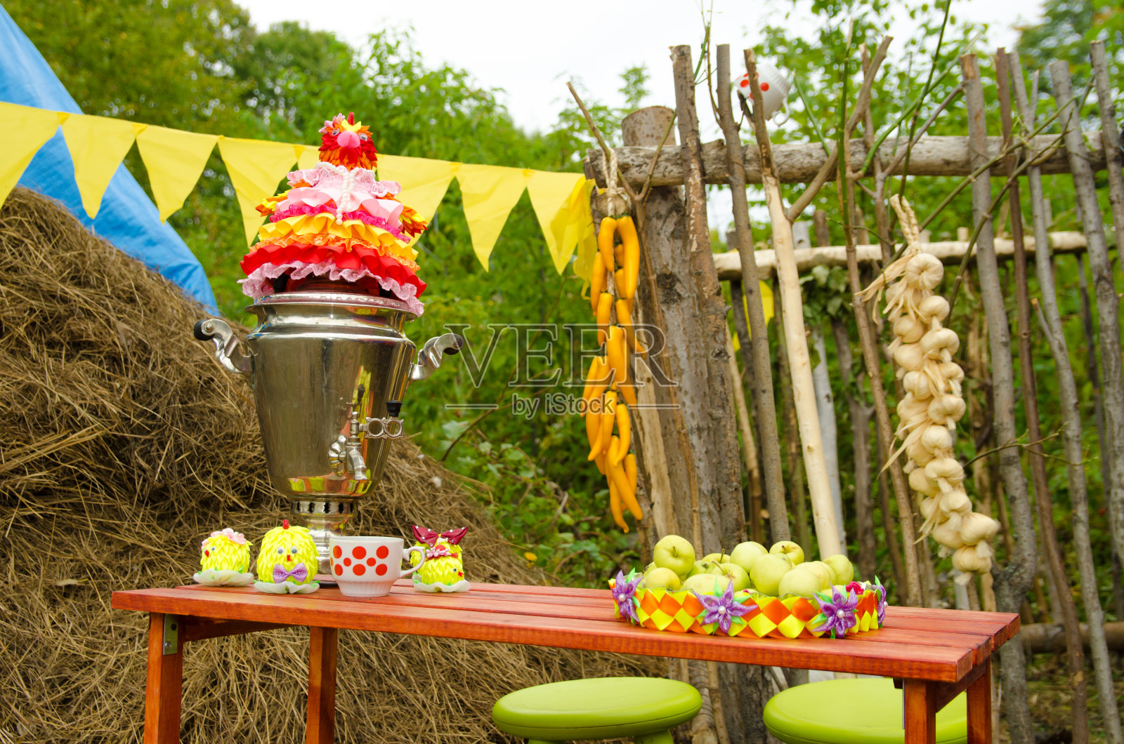 靠篱笆的木桌上放着茶炊、杯子和盛着苹果的盘子照片摄影图片