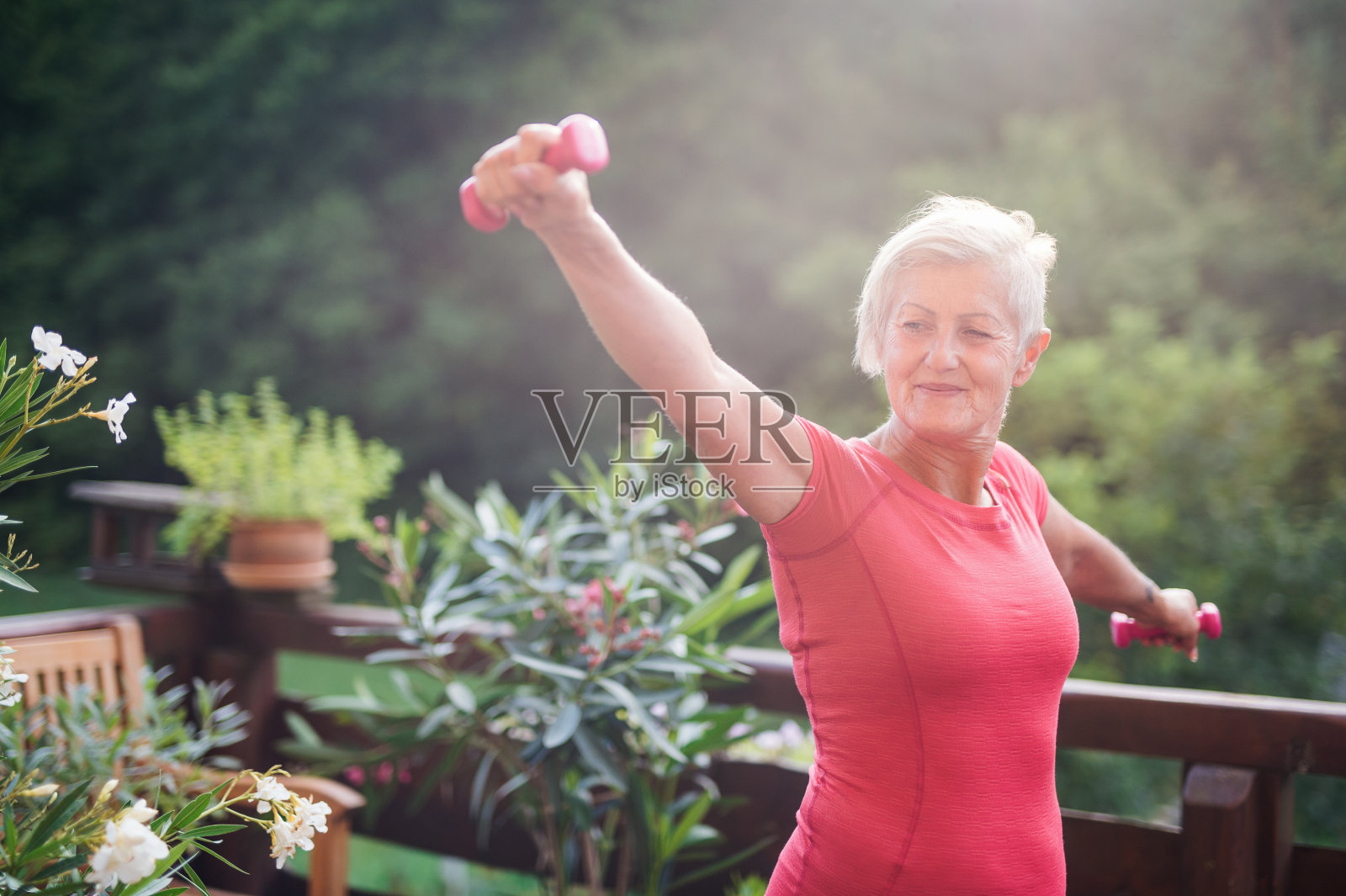 一位老年妇女站在户外的露台上，在夏天做运动。照片摄影图片