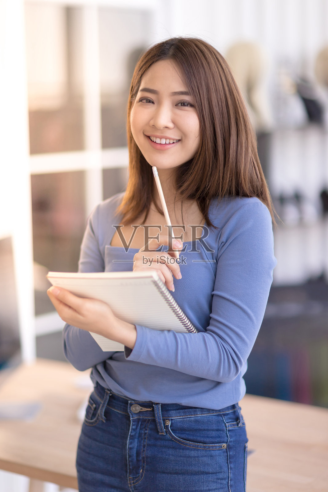 一个美丽的亚洲女人正站着，手里拿着一个笔记本，面带微笑照片摄影图片