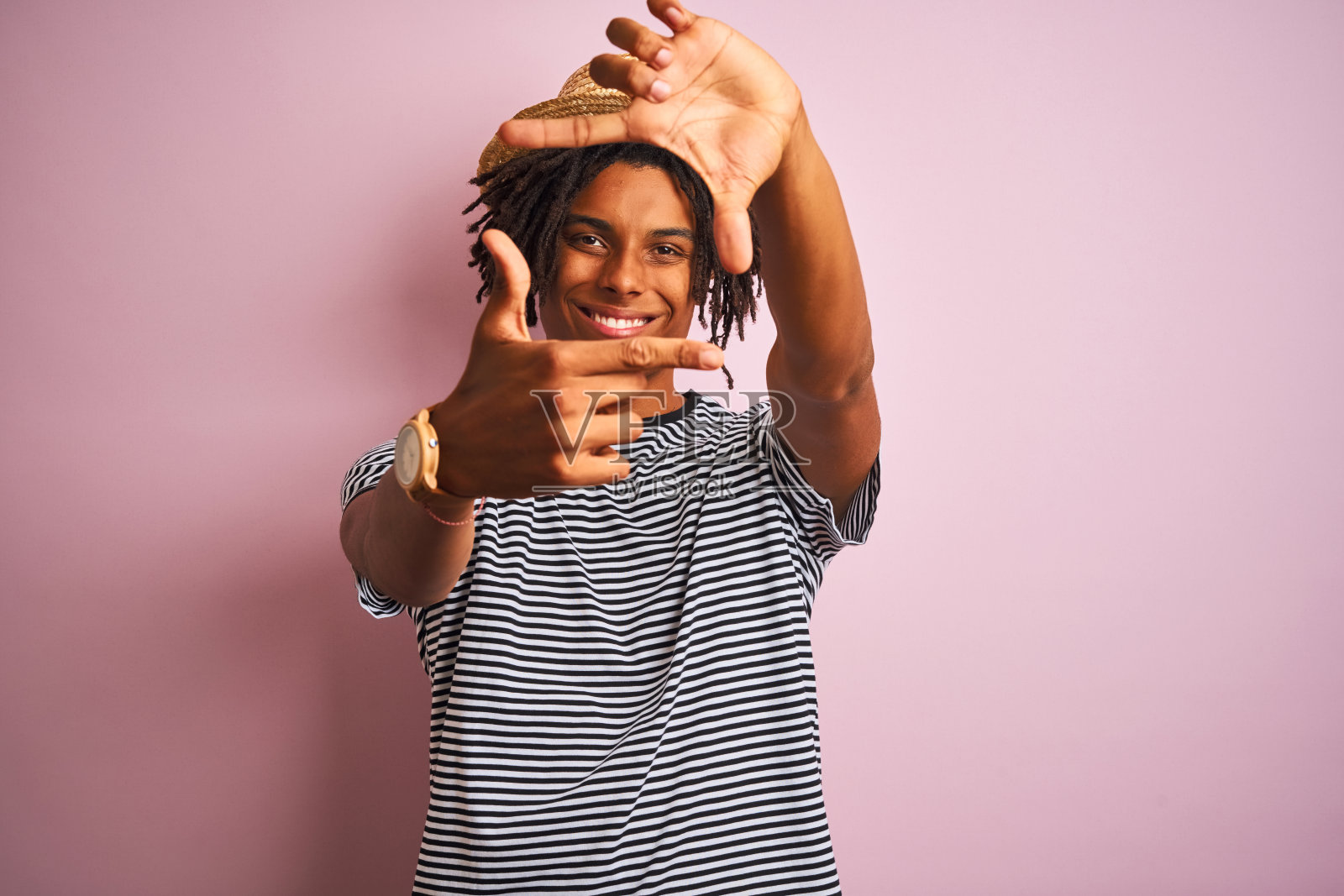 非洲裔美国人与雷鬼发穿着海军t恤和帽子在孤立的粉红色背景微笑做框架与手和手指与快乐的脸。创意和摄影概念。照片摄影图片