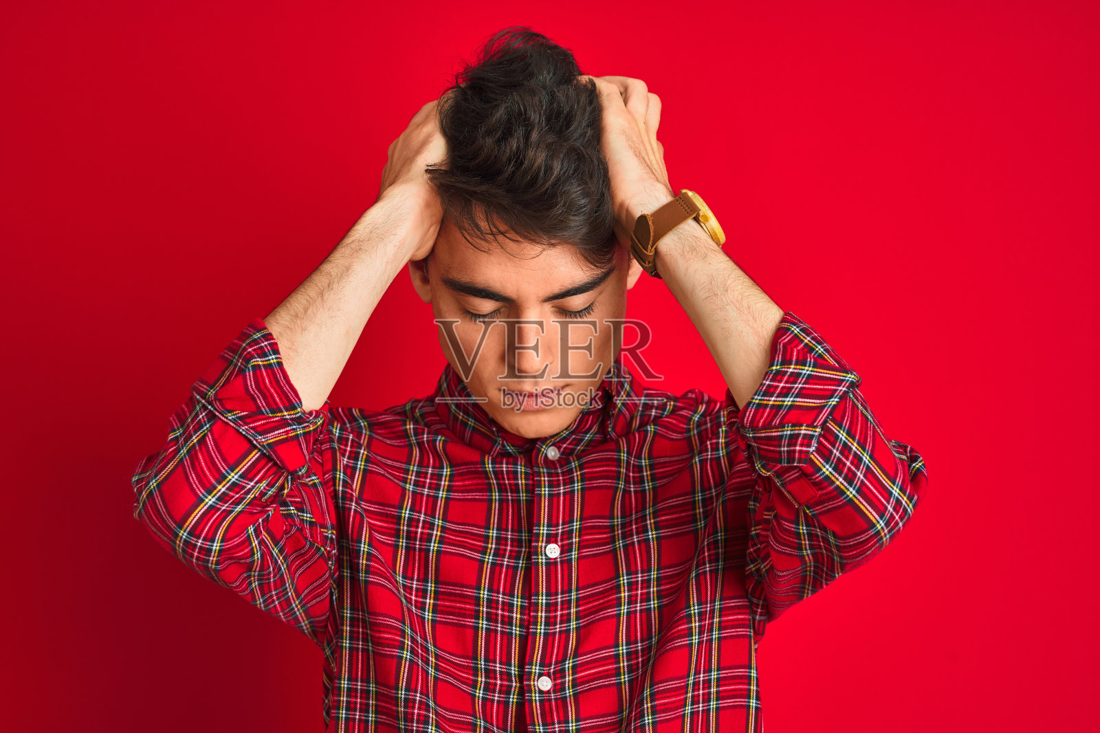 青少年男孩身穿红色衬衫，头痛欲裂，双手抱头，感到绝望和压力照片摄影图片