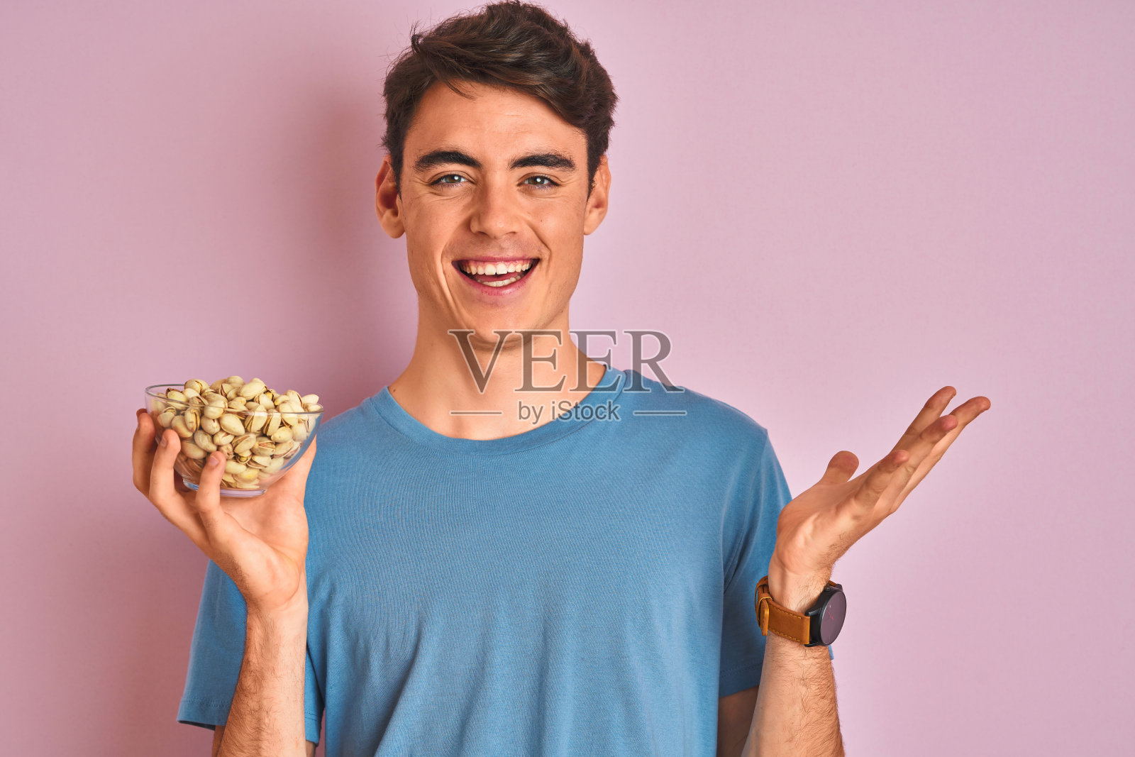 十几岁的男孩抱着一束开心果在孤立的粉红色背景非常高兴和兴奋，胜利者的表情庆祝胜利尖叫着大大的微笑和举起手照片摄影图片