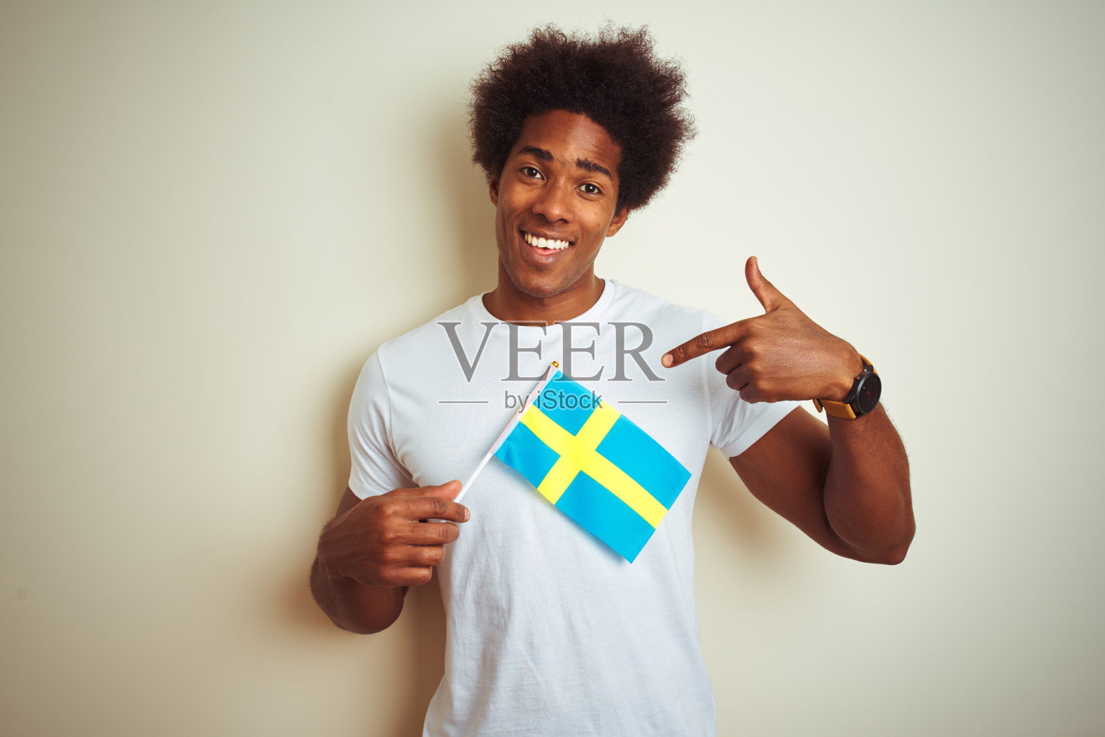 年轻的美国黑人男子举着瑞典瑞典国旗站在孤立的白色背景与惊讶的脸指向自己照片摄影图片