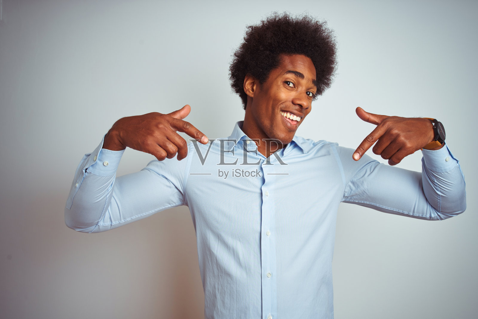 年轻的非洲裔美国人与非洲式的头发穿优雅的衬衫在孤立的白色背景看起来自信的微笑在脸上，用手指指着自己骄傲和幸福。照片摄影图片