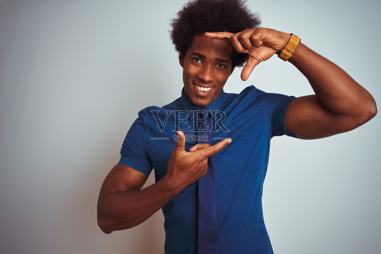 美国商人与非洲式头发穿蓝色衬衫和领带在孤立的白色背景微笑做框架与手和手指与快乐的脸。创意和摄影概念。照片摄影图片