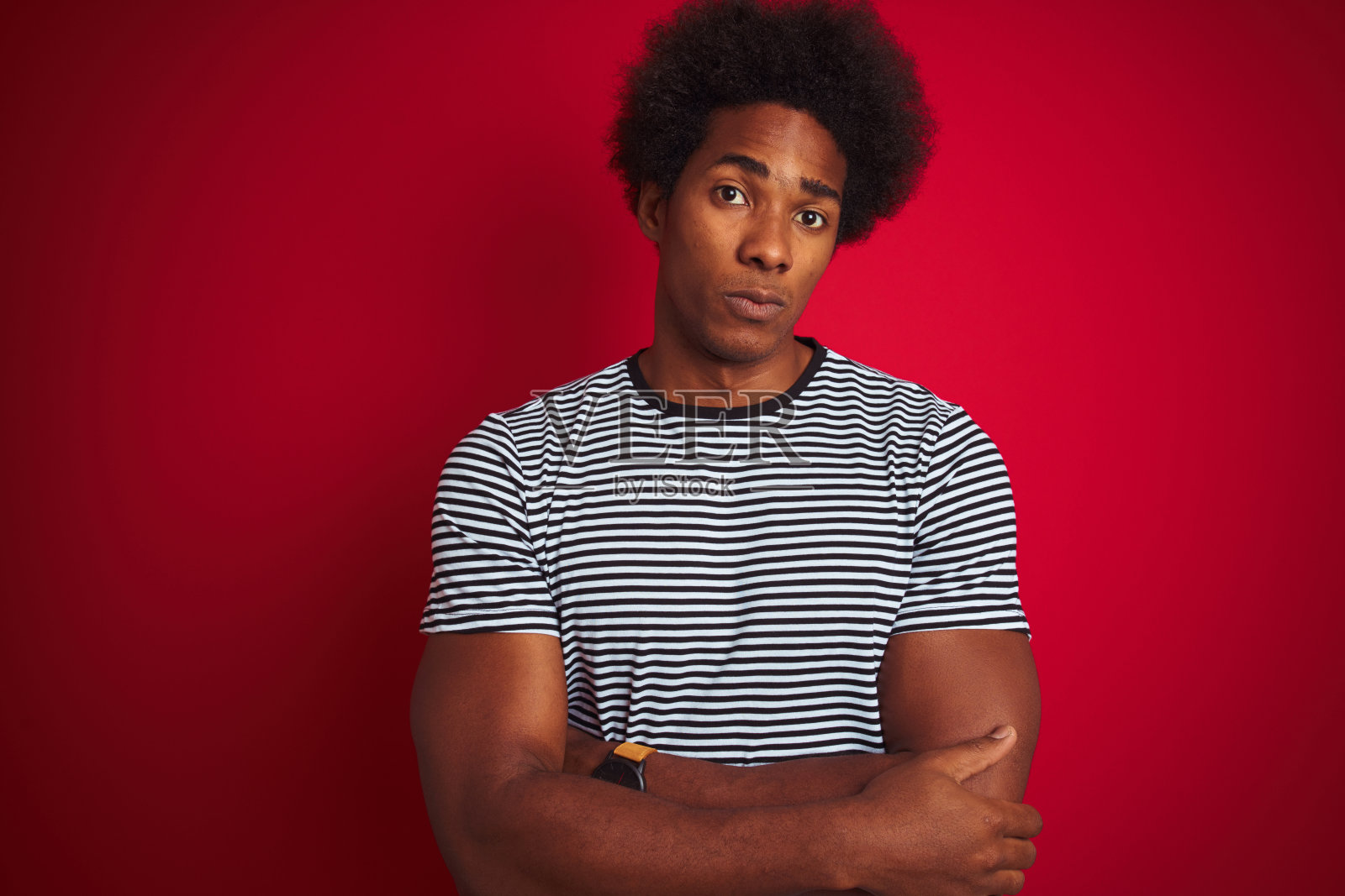 年轻的美国人与非洲式头发穿海军蓝条纹t恤在孤立的红色背景怀疑和紧张，不赞成的表情在脸上交叉双臂。消极的人。照片摄影图片