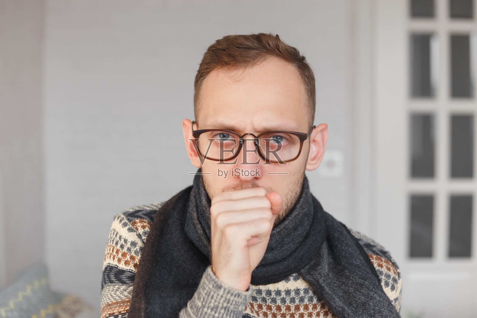 一个脖子上围着围巾的年轻人因为感冒和喉咙痛而咳嗽照片摄影图片