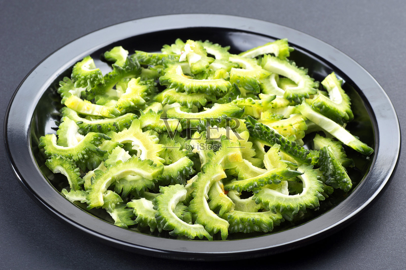 苦瓜或苦瓜放在黑色的盘子上，背景是黑色的。照片摄影图片