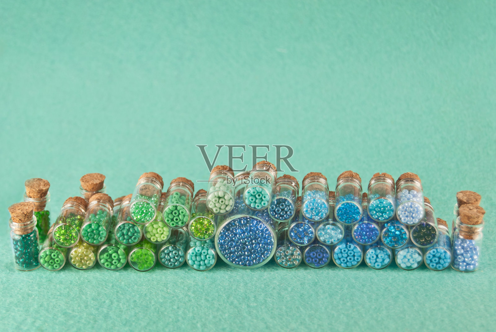 蓝色，绿色，黄色和紫色的珠子在明亮的青色背景玻璃罐。带木塞的透明容器中的珠子。有序，平衡和混乱的概念。照片摄影图片