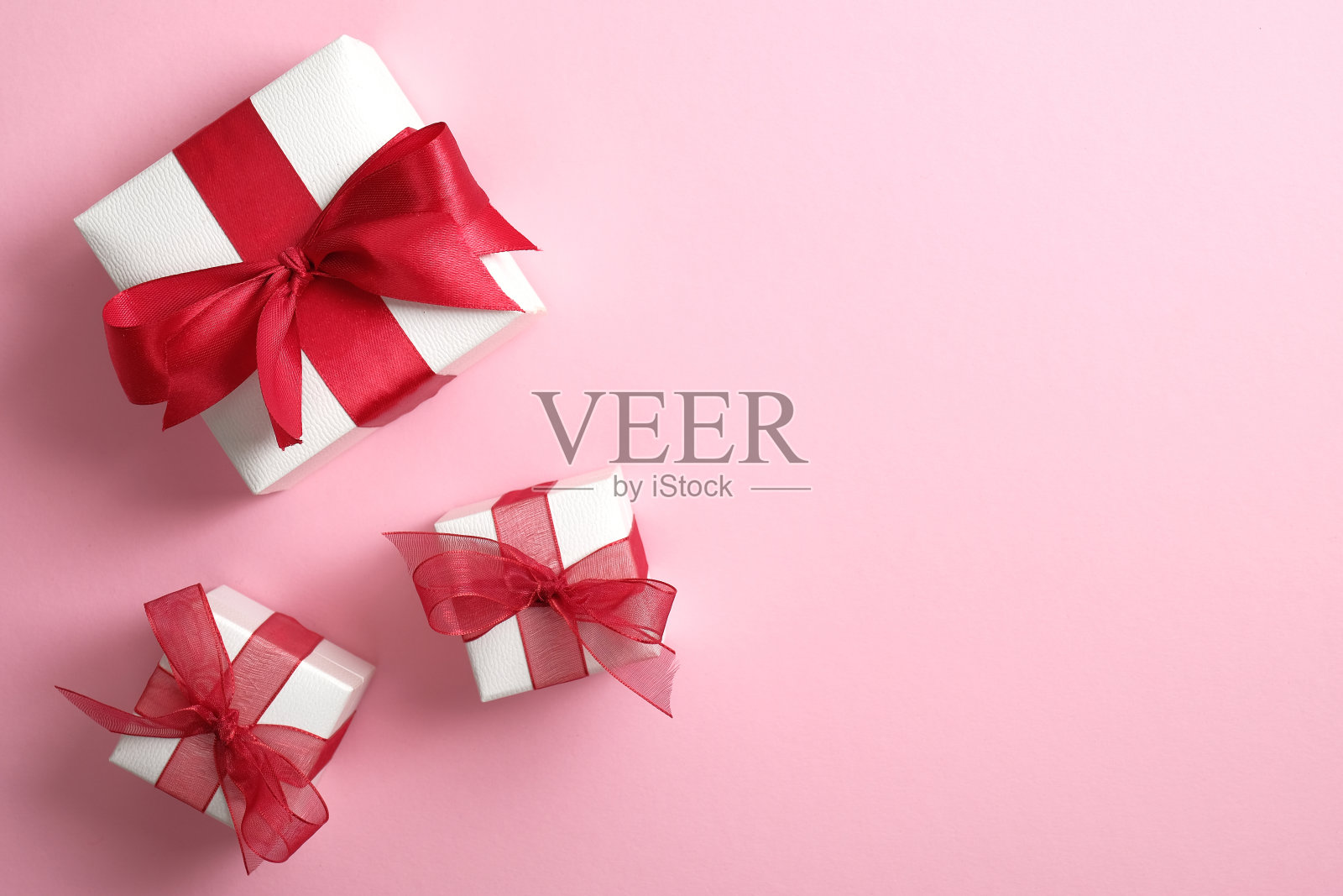 白色礼盒与红色丝带蝴蝶结在柔和的粉红色背景。情人节惊喜，爱的概念。平躺，俯视图。照片摄影图片