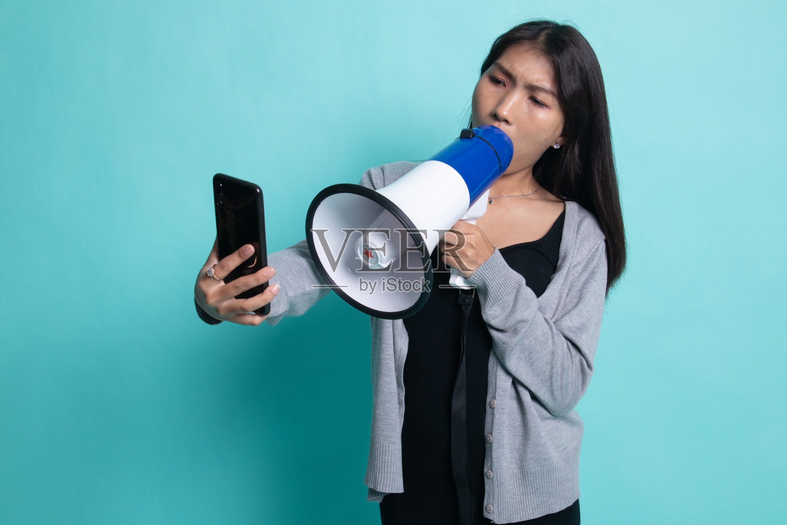 愤怒的年轻亚洲女子用扩音器对着手机大喊。照片摄影图片