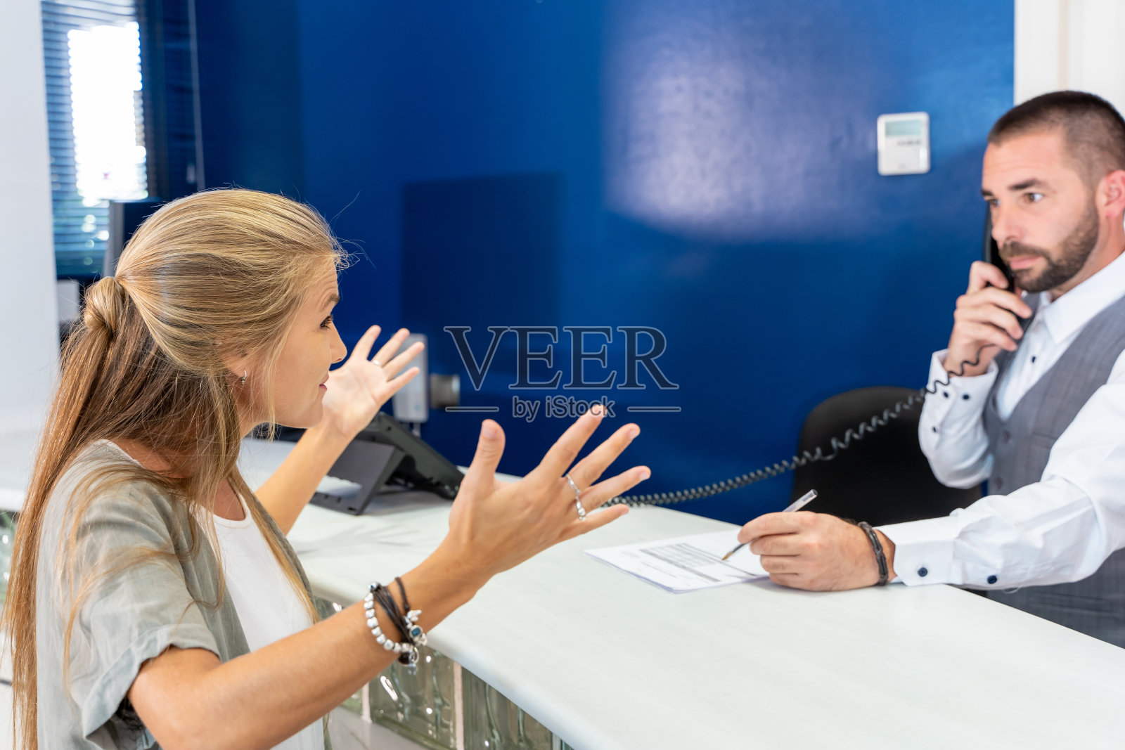 年轻的金发女郎在酒店门口做手势，酒店接待员在接电话照片摄影图片