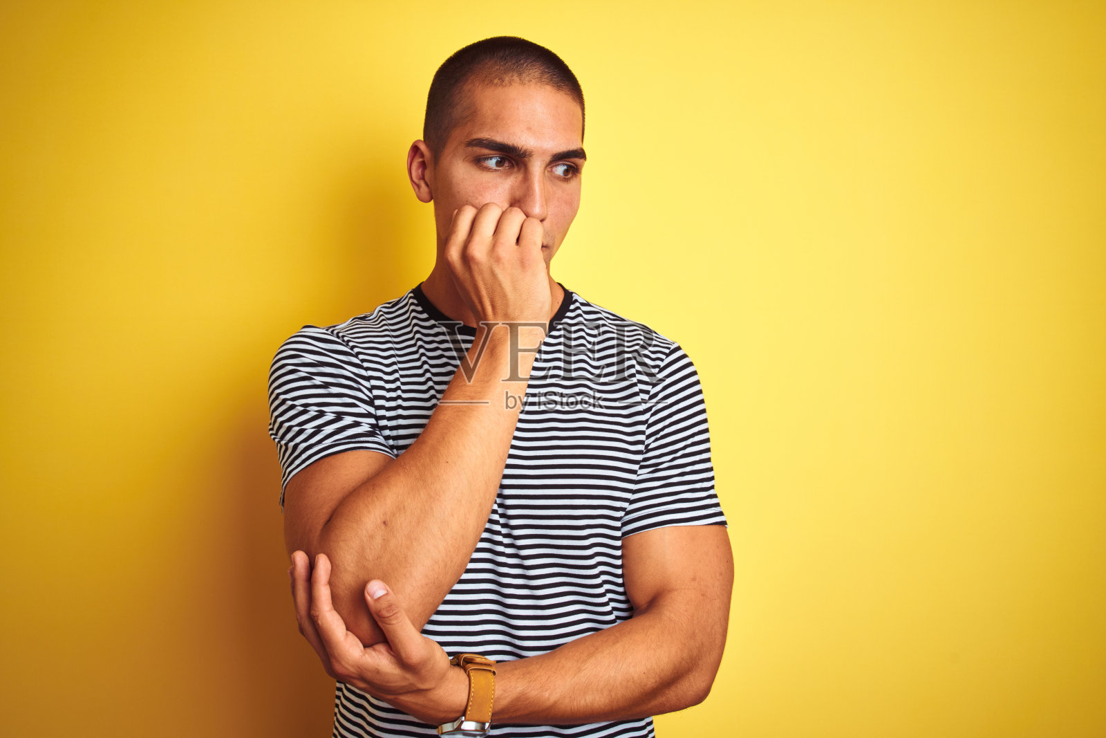 年轻英俊的男子穿着条纹t恤在黄色孤立的背景看起来紧张和紧张与手在嘴咬指甲。焦虑的问题。照片摄影图片
