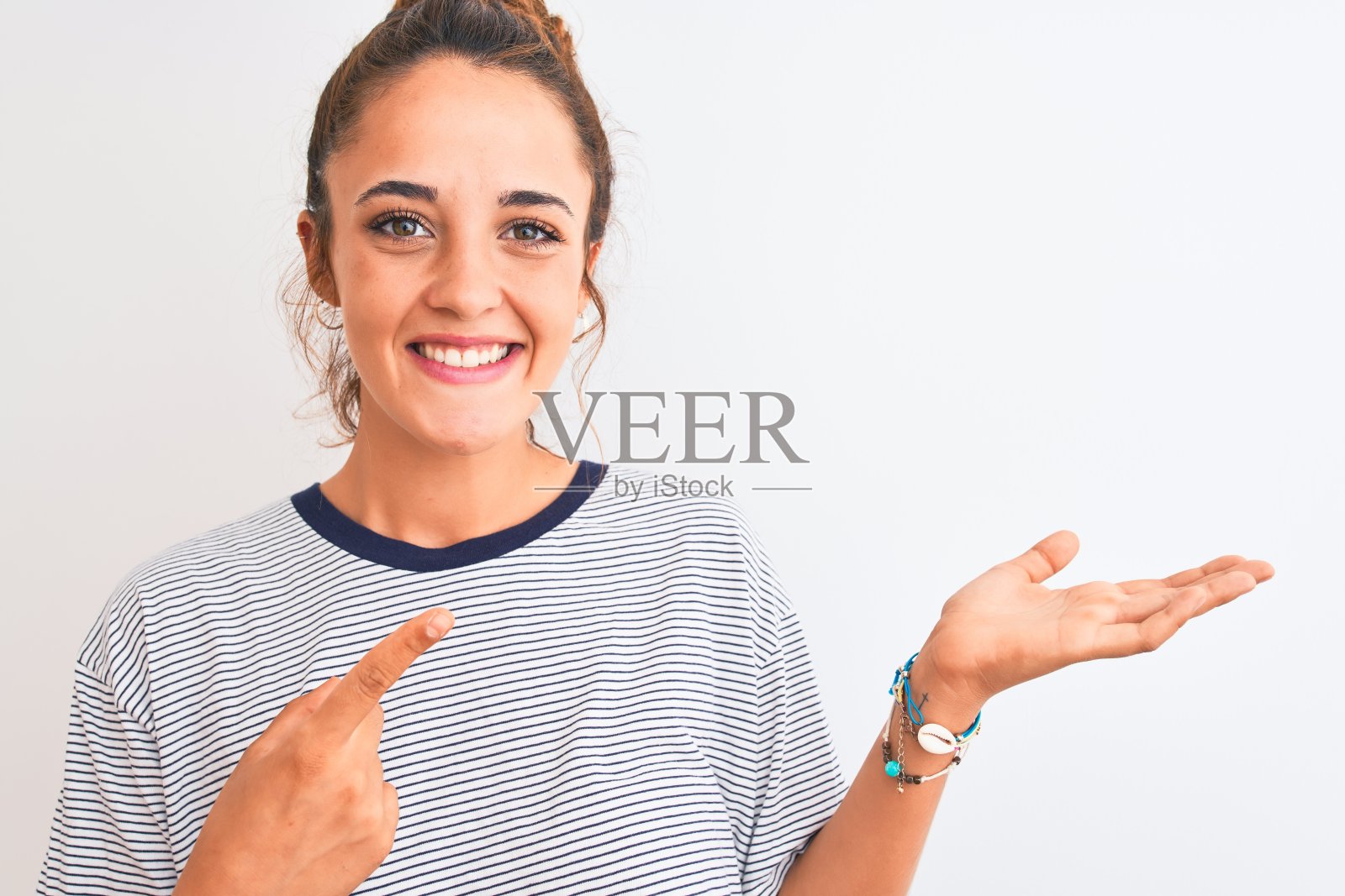 年轻的红头发的现代女性在孤立的背景下梳着一个发髻，非常高兴地用手和手指指着照片摄影图片