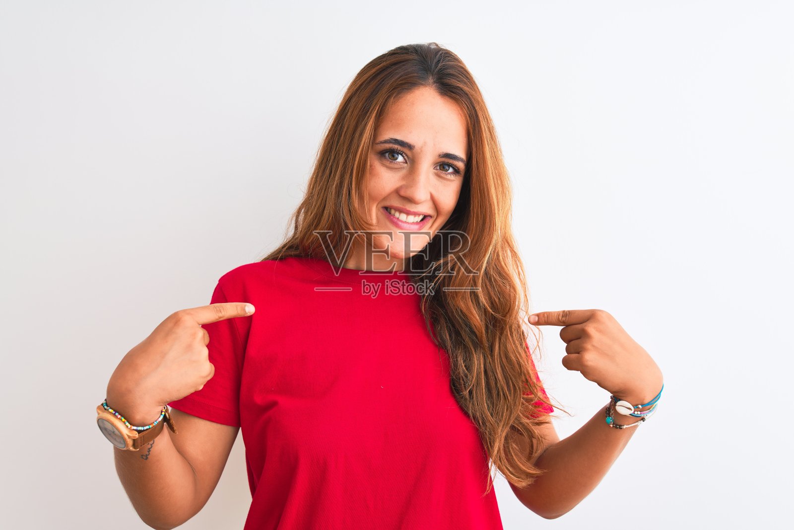 年轻的红发女子穿着红色休闲t恤站在白色孤立的背景看起来自信与微笑的脸上，用手指指着自己骄傲和幸福。照片摄影图片
