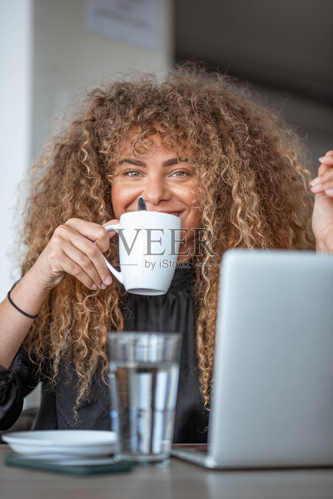 在一张咖啡馆的库存照片中，一个年轻女子一边喝着白色的茶杯，一边在用笔记本电脑工作照片摄影图片