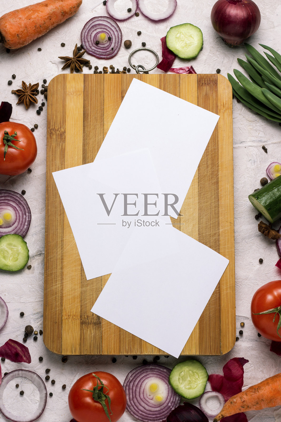 在切菜板和一个有拷贝空间的笔记本周围放着新鲜的农场蔬菜。西红柿，红洋葱圈，香料，黄瓜，胡萝卜。做饭的场景照片摄影图片
