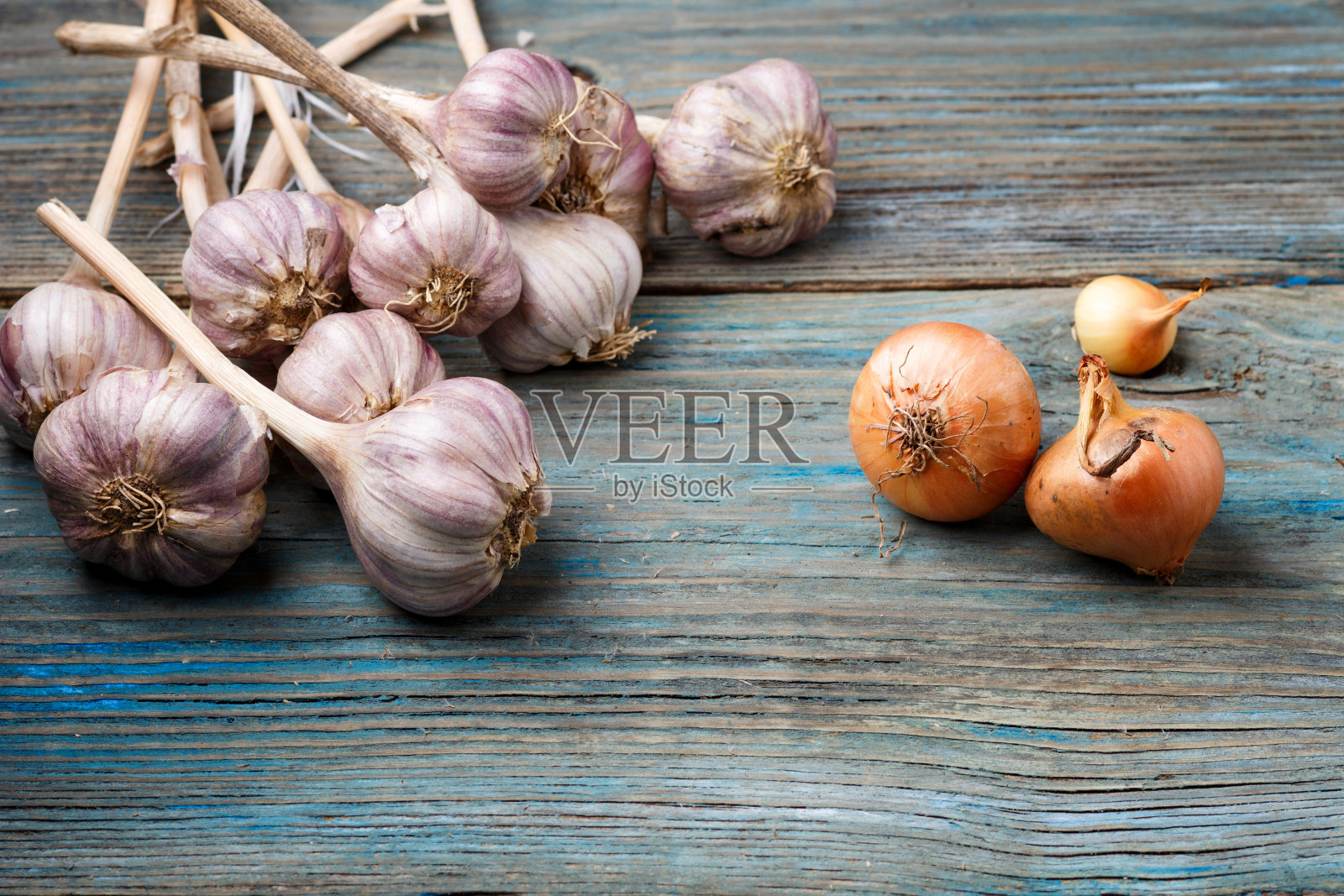 新鲜的紫罗兰色大蒜和橙色的洋葱在蓝色的乡村木制背景上。对比的概念。照片摄影图片