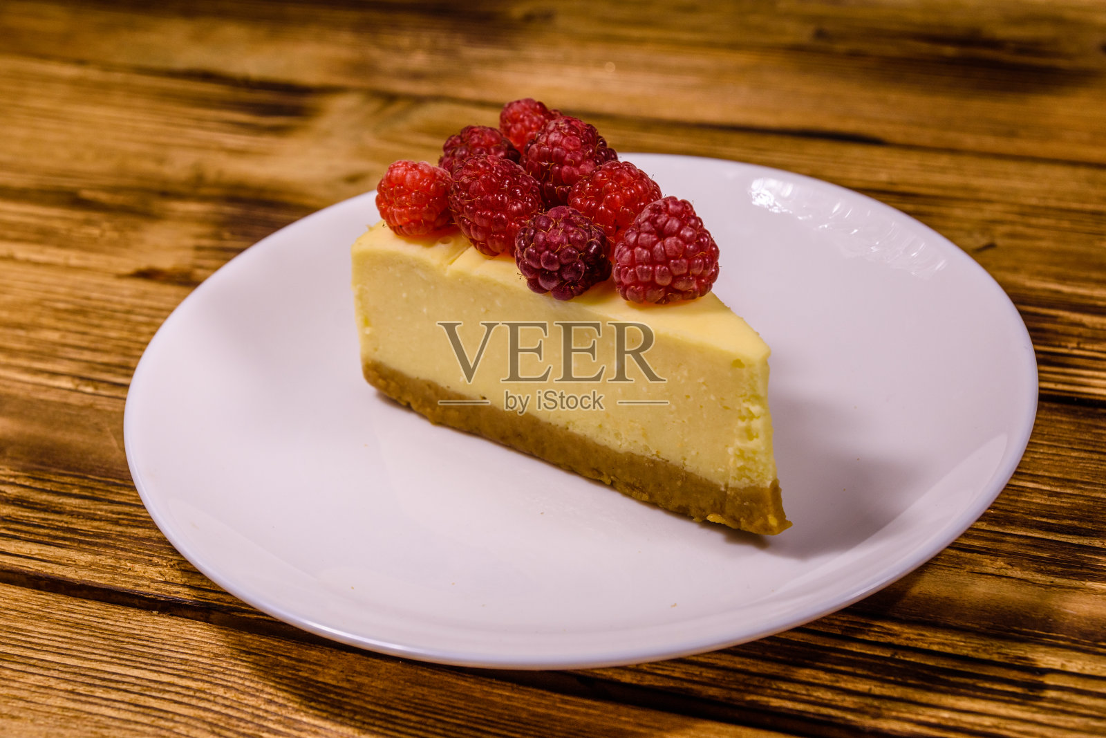白色盘子上有纽约奶酪蛋糕和木桌子上的覆盆子照片摄影图片