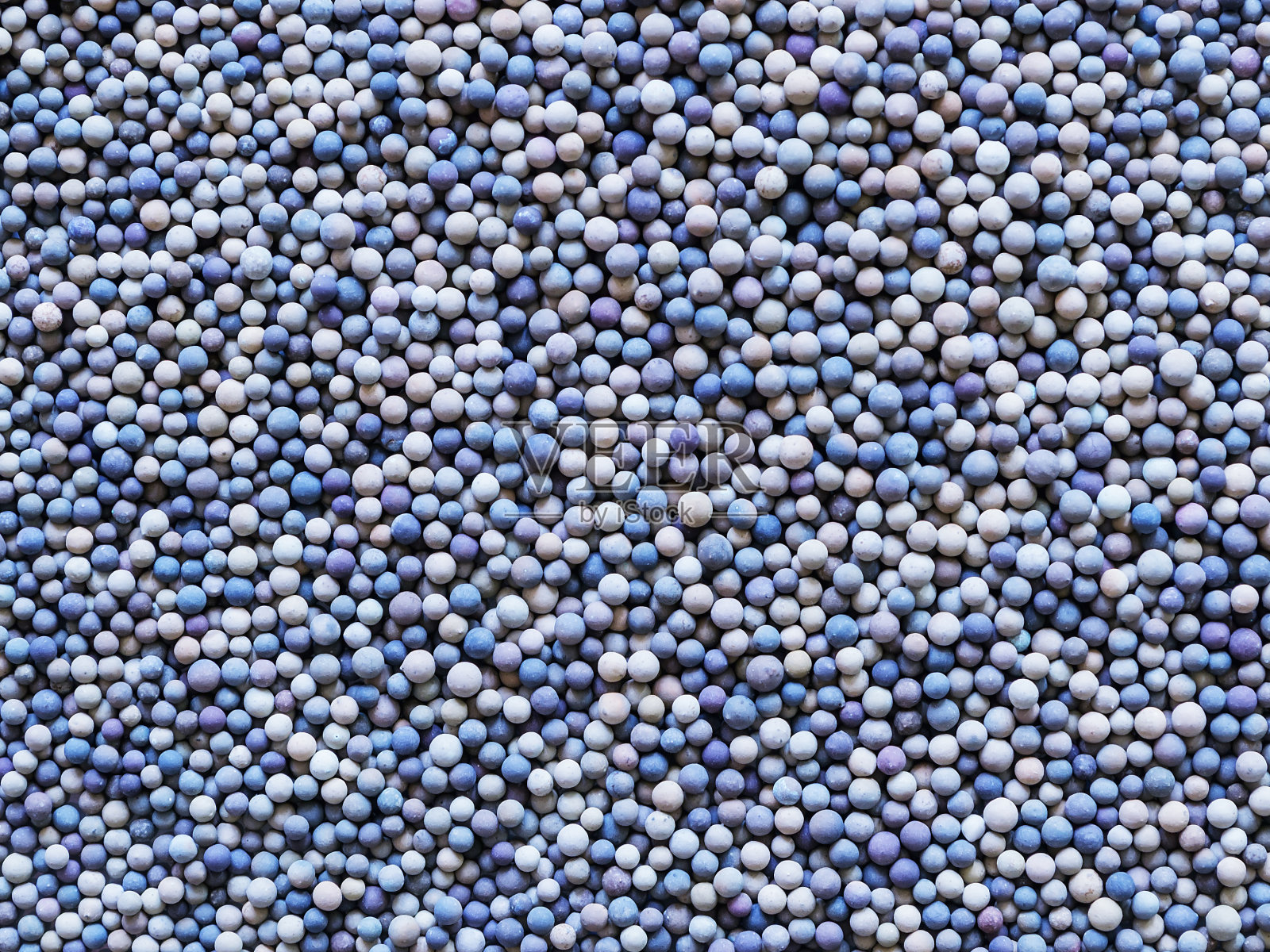 许多微小的陶瓷球或颗粒的颜色范围从米色到深蓝色作为背景。粒状或粒状结构。照片摄影图片