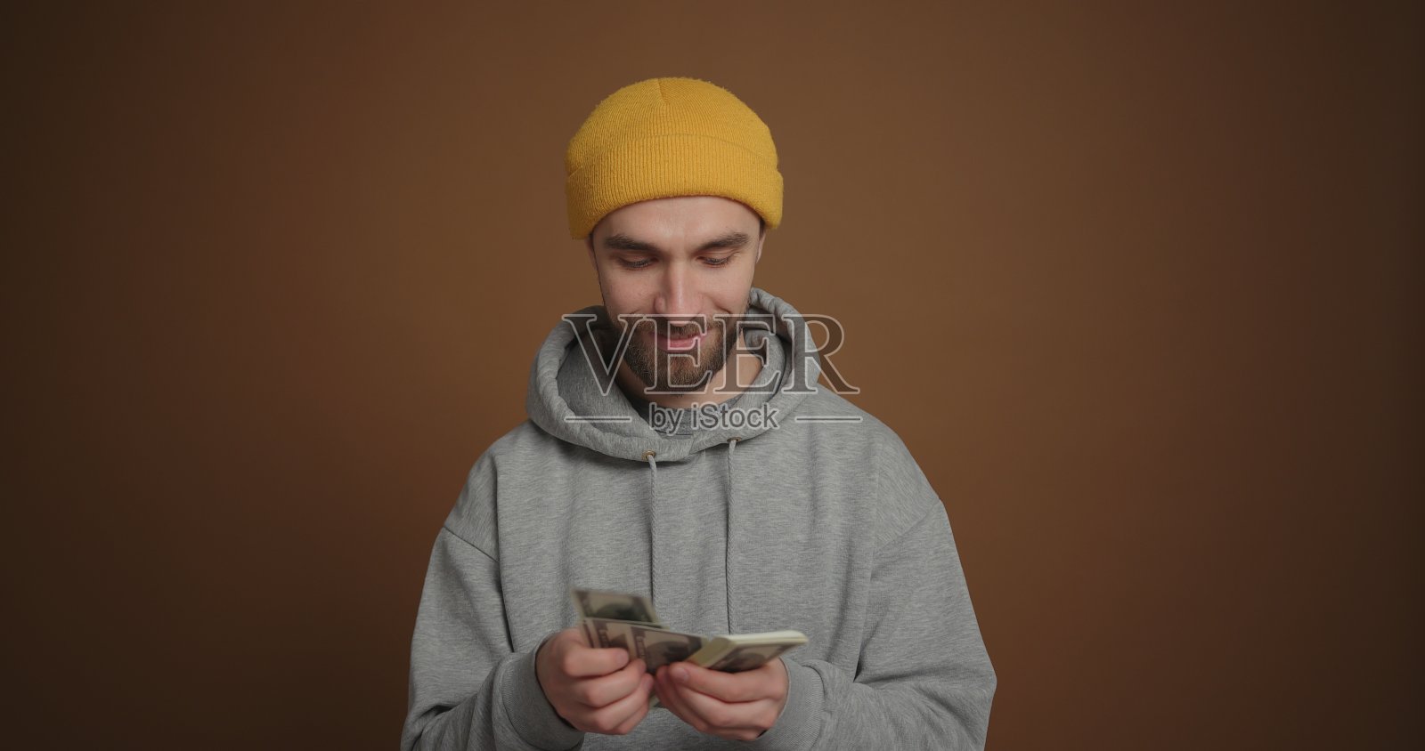 戴黄帽子的满意男子在棕色背景下数现金照片摄影图片