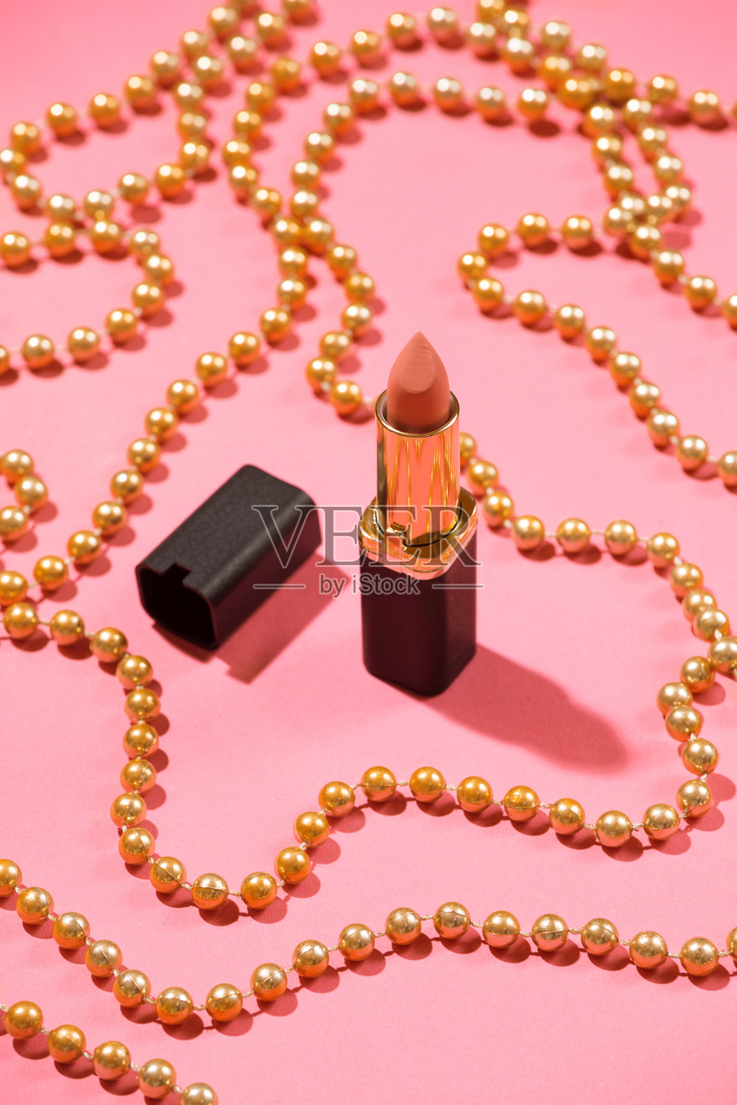 裸色唇膏以粉色背景装饰金色节日珠子。照片摄影图片
