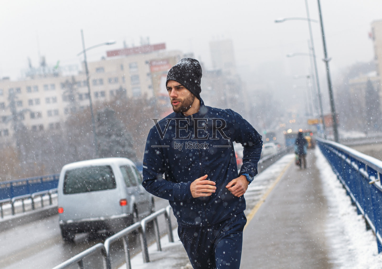 在寒冷的冬天，一个年轻人在城市的街道上奔跑。照片摄影图片