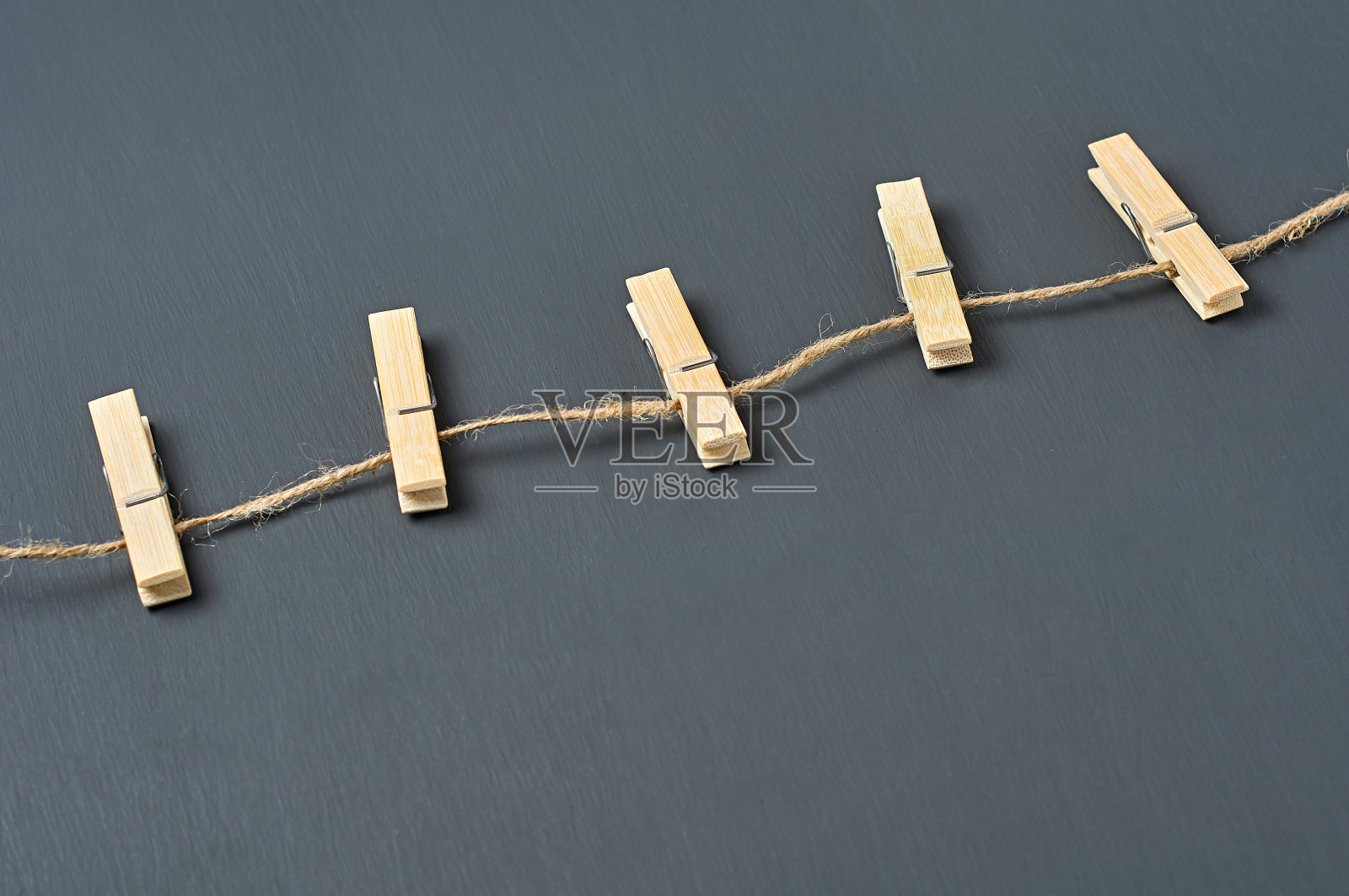深色混凝土背景上的晒衣绳和五个木制晒衣夹。特写镜头照片摄影图片